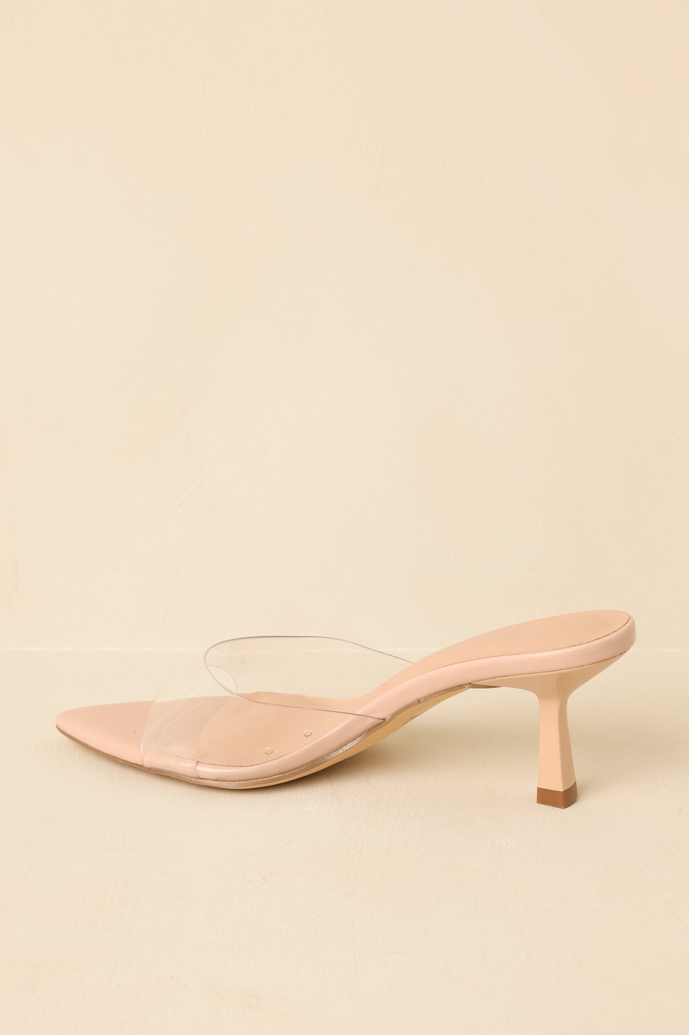 Back view of nude kitten heel mules showing the low heel, clear strap, and pointed toe from behind.