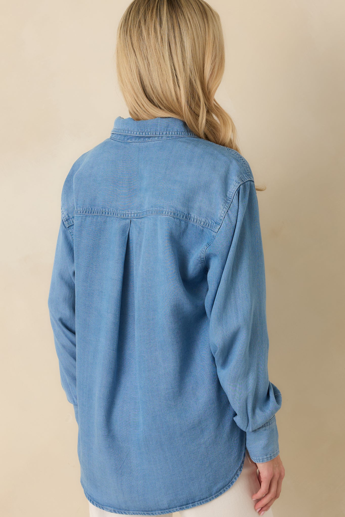 Back view of the medium wash denim button-up shirt showing the relaxed silhouette and gently curved hem.