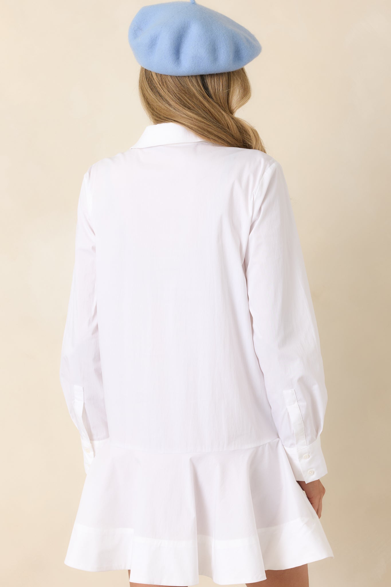 Back view of the white shirt-style mini dress showing smooth back panel, long sleeves, and softly flared hem.