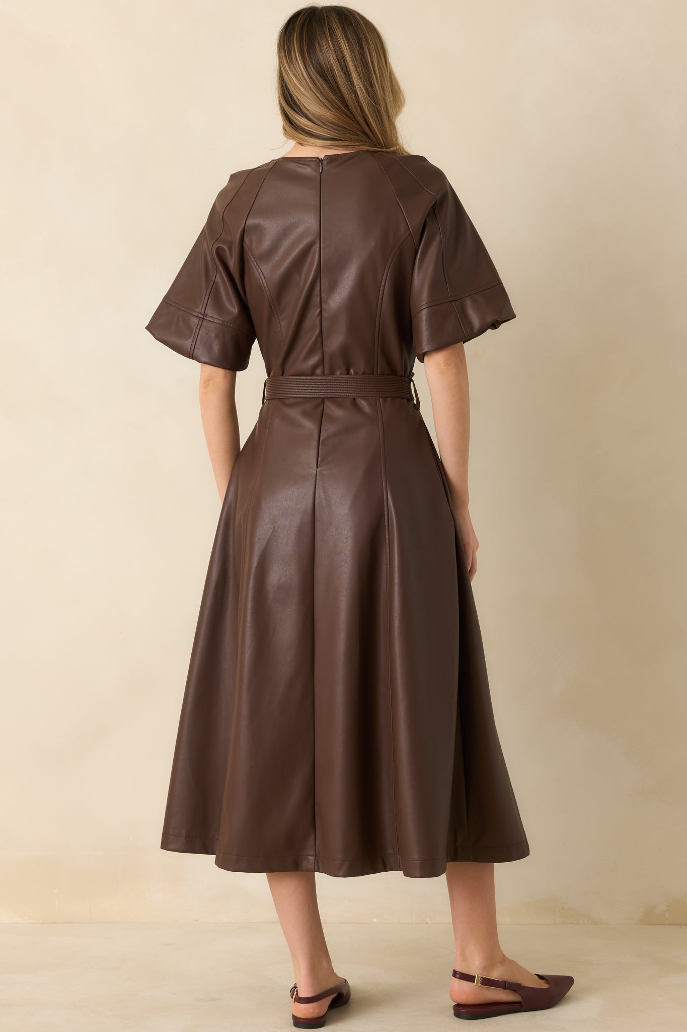 Back view of brown midi dress showing smooth faux leather finish, raglan sleeves, and gathered waist tie.