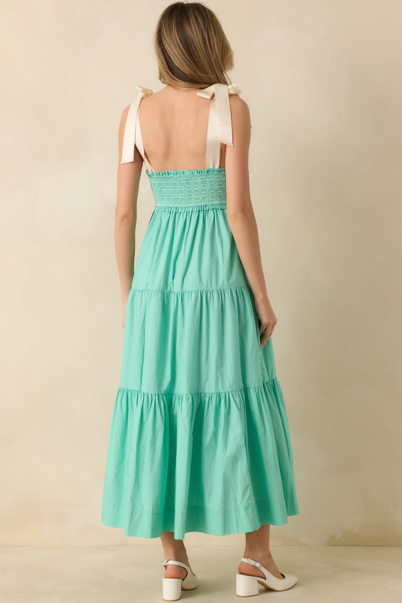 Back view of mint green midi dress showing the smocked construction, ivory tie straps, and flowing skirt with pockets.
