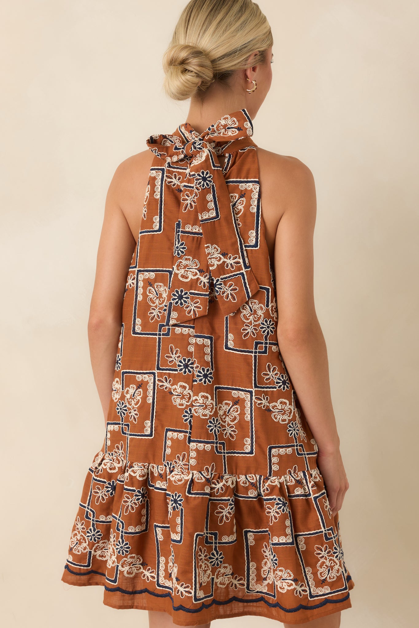 Back view of the terracotta halter mini dress featuring a tied bow neckline and flowing silhouette.