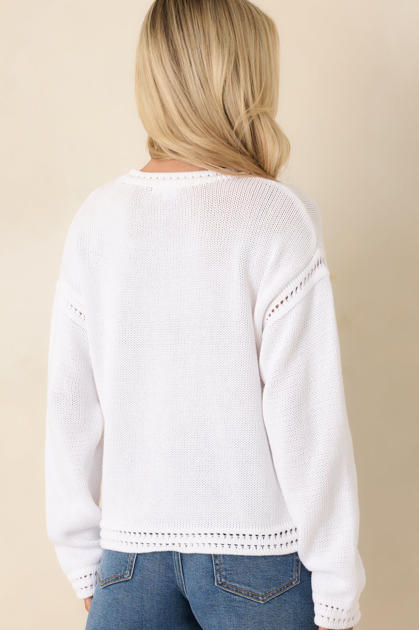 Back view of white cotton knit sweater with long sleeves, ribbed hem, and subtle textured stitch accents along the shoulders.