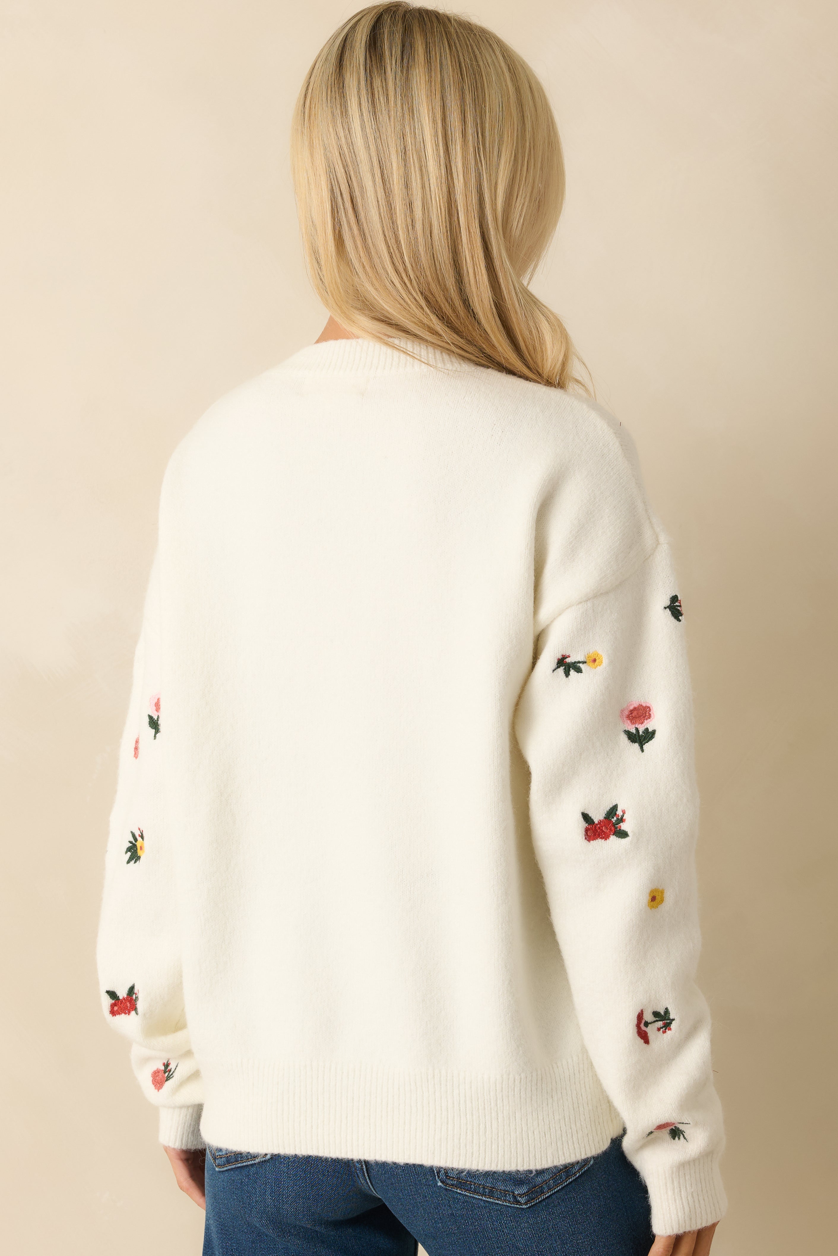 Rear view of the white knit sweater showing floral embroidery and ribbed hemline.