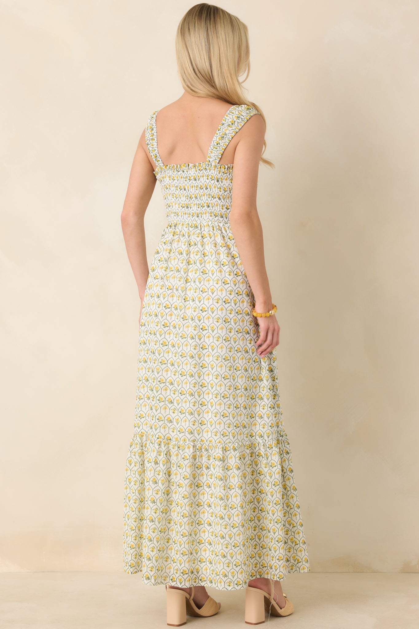 Back view of yellow floral maxi dress featuring the fully smocked bodice, wide shoulder straps, and flowing tiered skirt.
