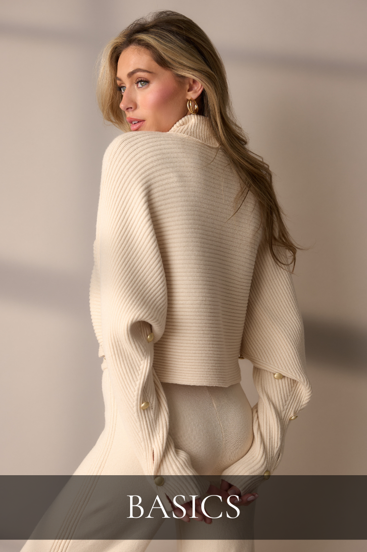 Woman wearing a cream ribbed knit sweater and matching pants with gold button details, linking to the Basics shop.