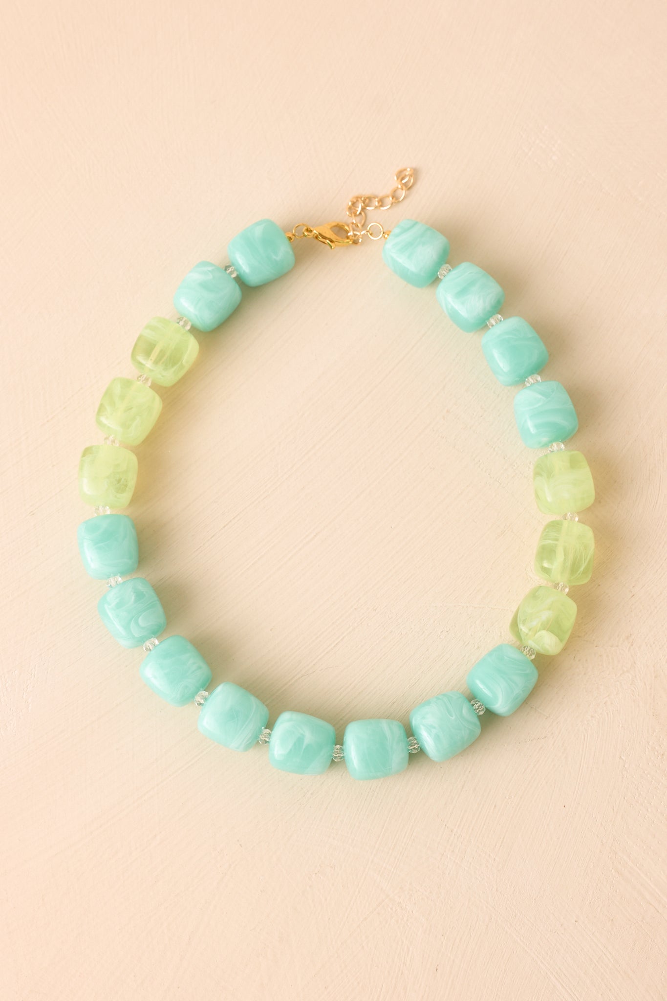 Marbled aqua and light green resin bead necklace displayed on a beige background, featuring a lightweight silhouette and gold-tone clasp closure.