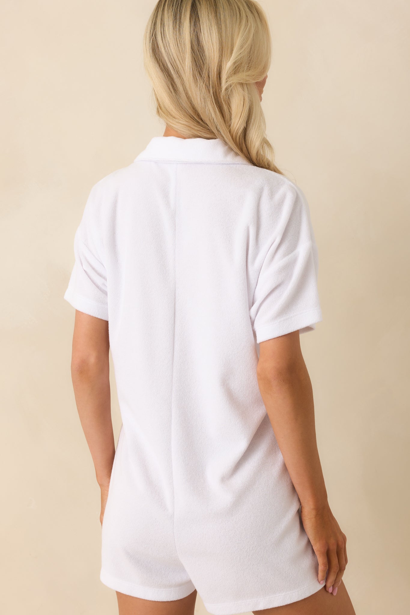 A view from behind of the white romper, displaying the short sleeves, collared neckline, and overall shape.