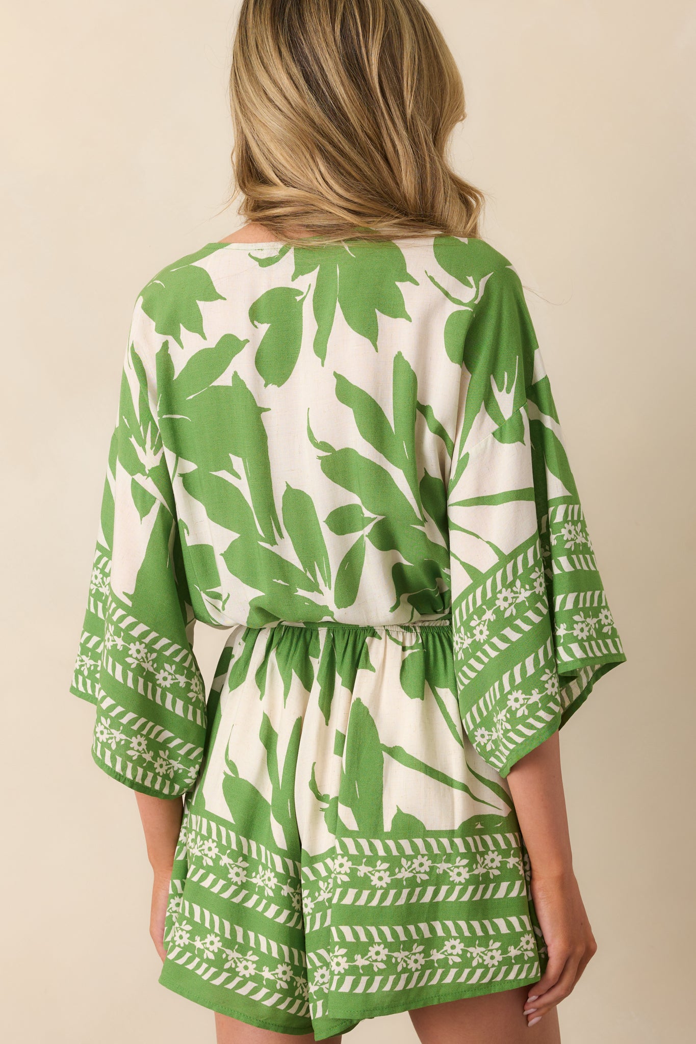 A view from behind showing the ivory and green floral print, relaxed fit, and contrast hem detail on the romper.