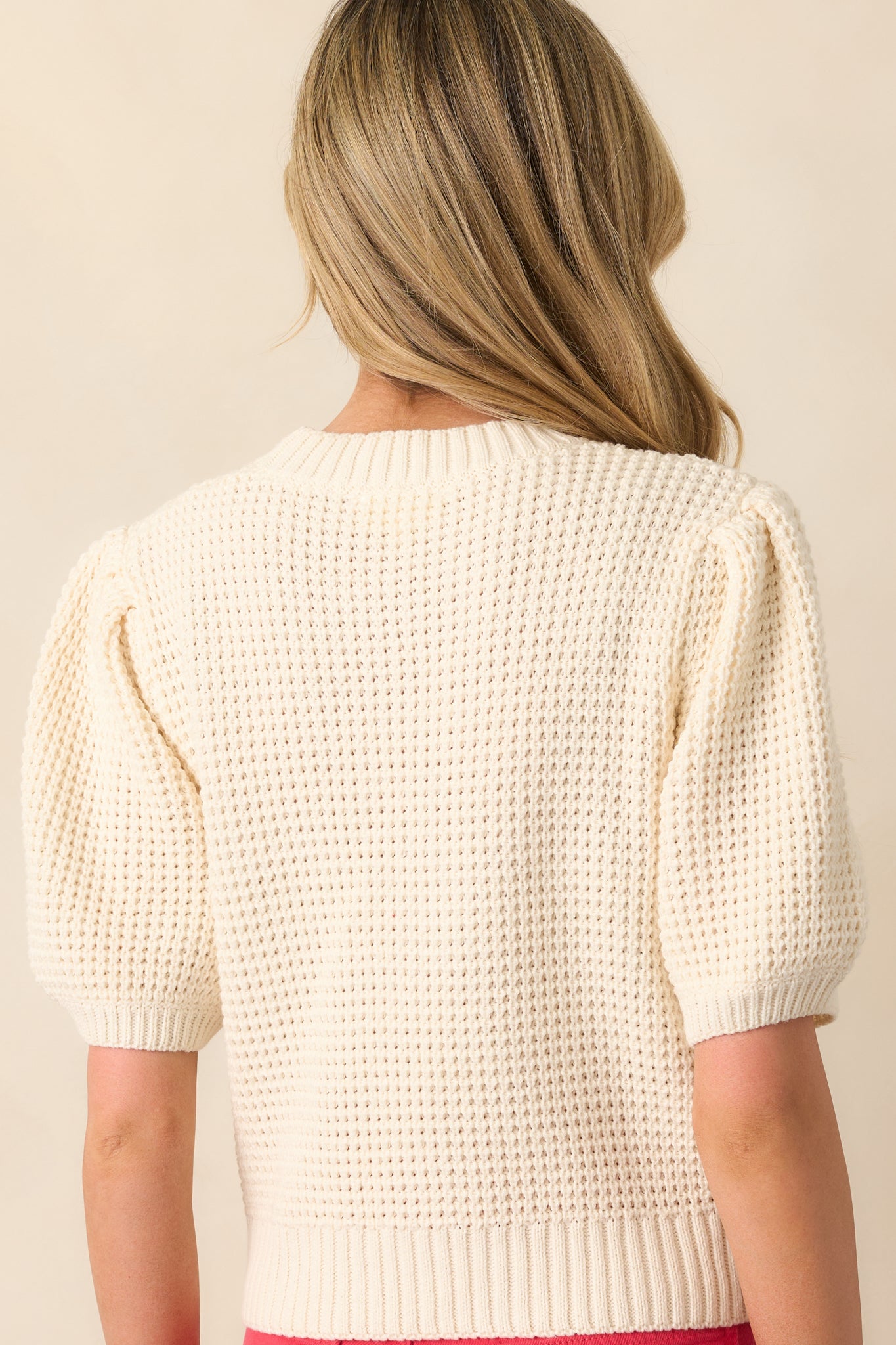 A view from behind showing the smooth knit texture, short sleeves, and ribbed hem of the ivory sweater.