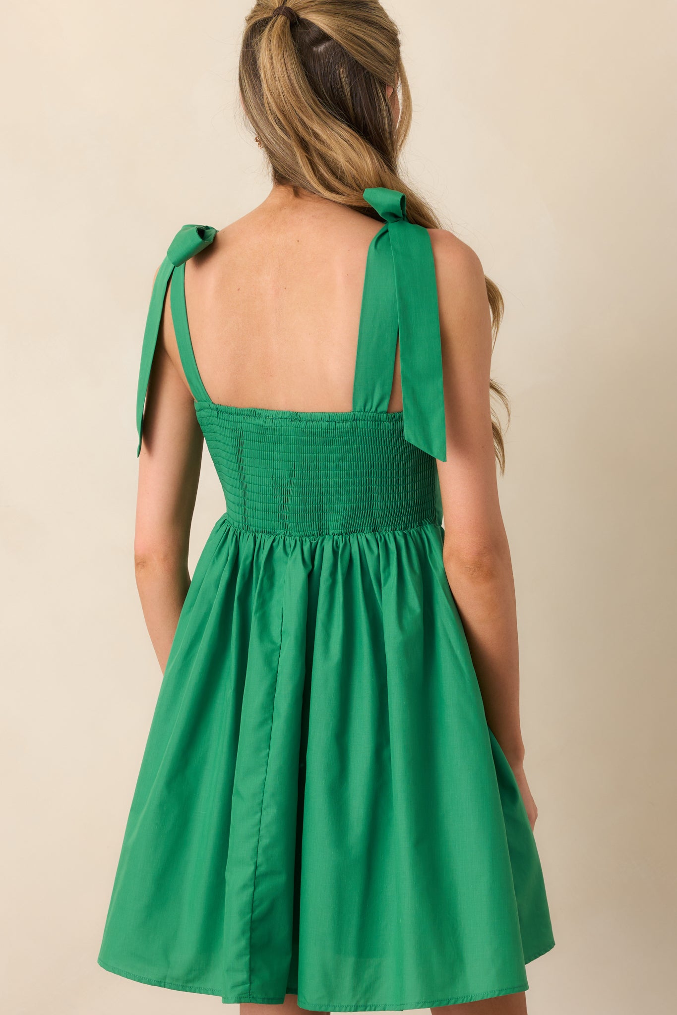 A view from behind showing smocked panel, white trim accents, and flowy skirt of the green mini dress.