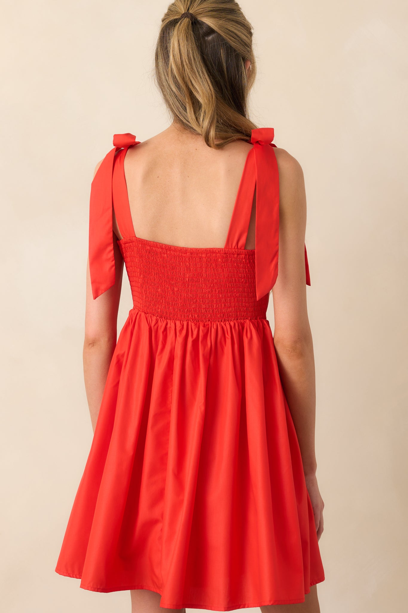 A view from behind showing smocked panel, pink trim accents, and flowy skirt of the red mini dress.