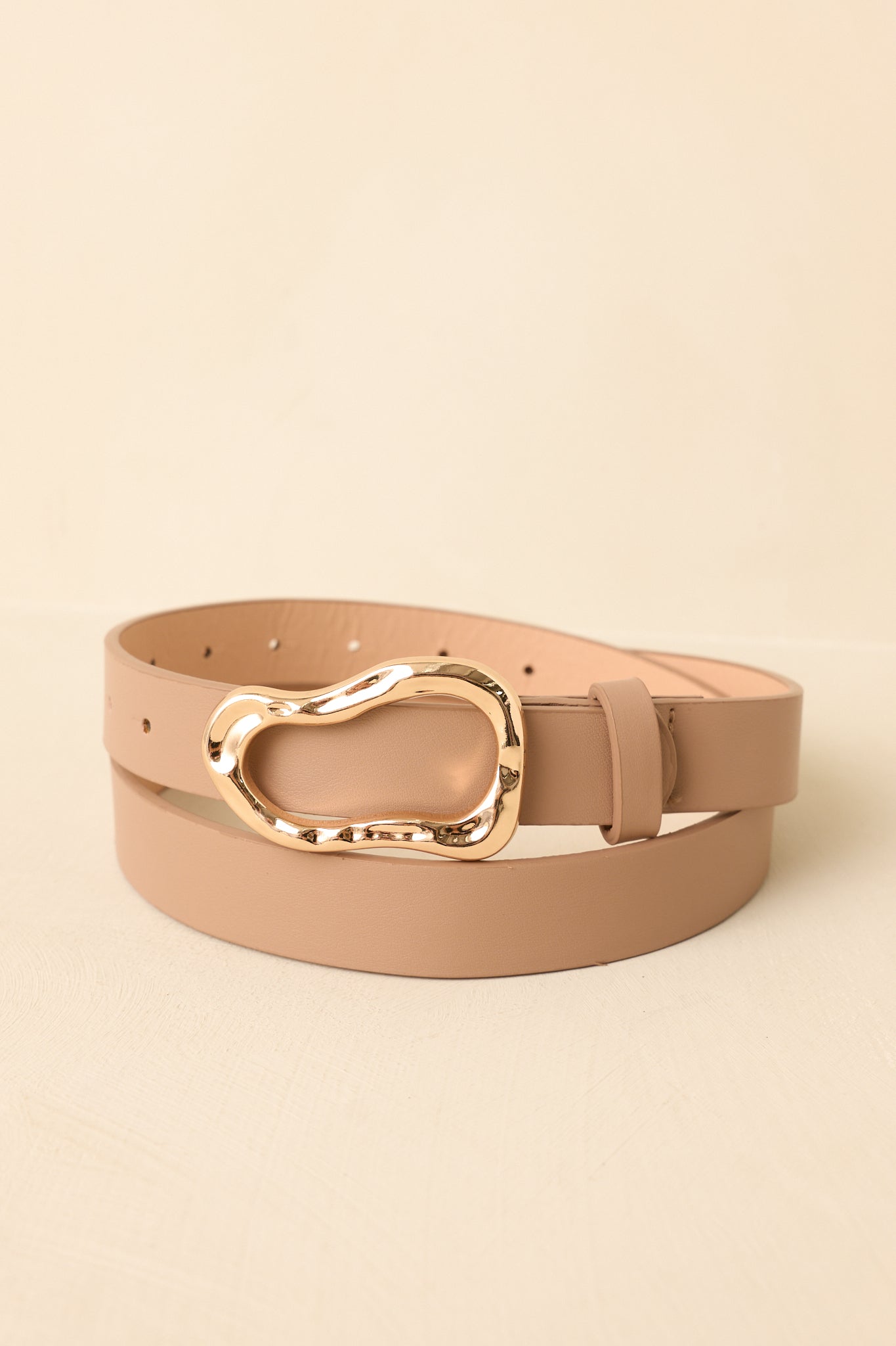 Cropped view of beige faux leather belt featuring a sculpted organic gold buckle and smooth neutral strap.