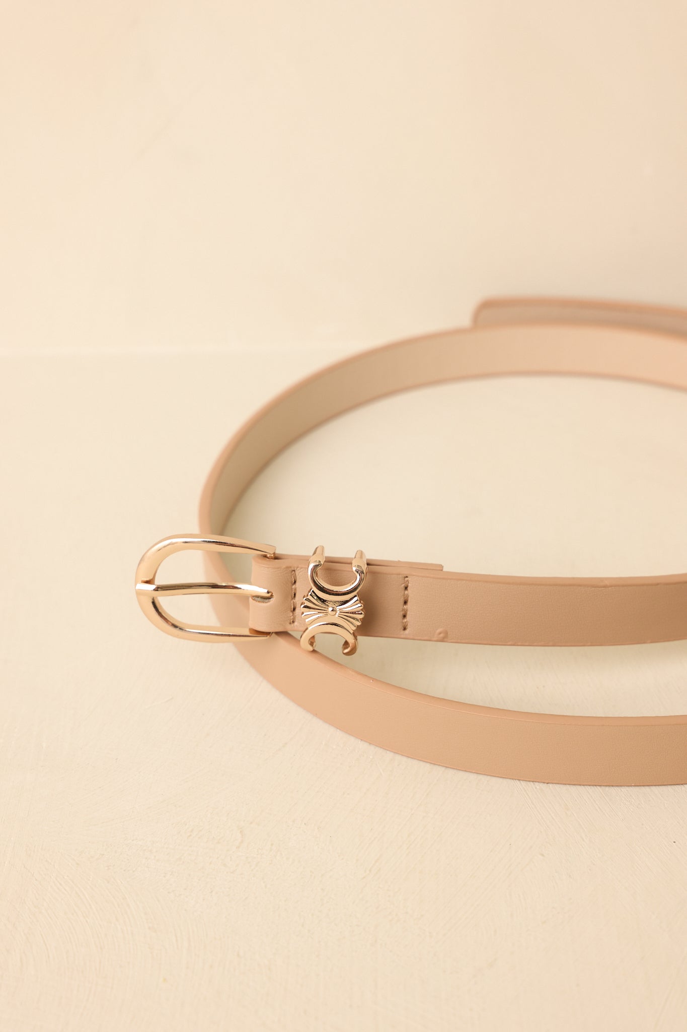 Detailed close-up of beige belt showcasing polished gold-tone buckle and refined faux leather texture.