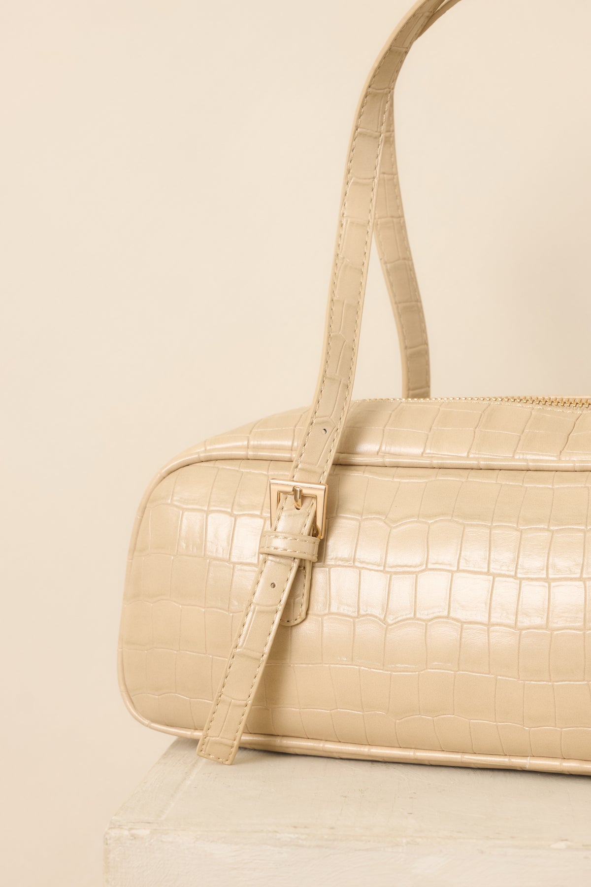 Close view of the handbag’s textured faux crocodile exterior, zipper closure, and neatly constructed top handle attachments.
