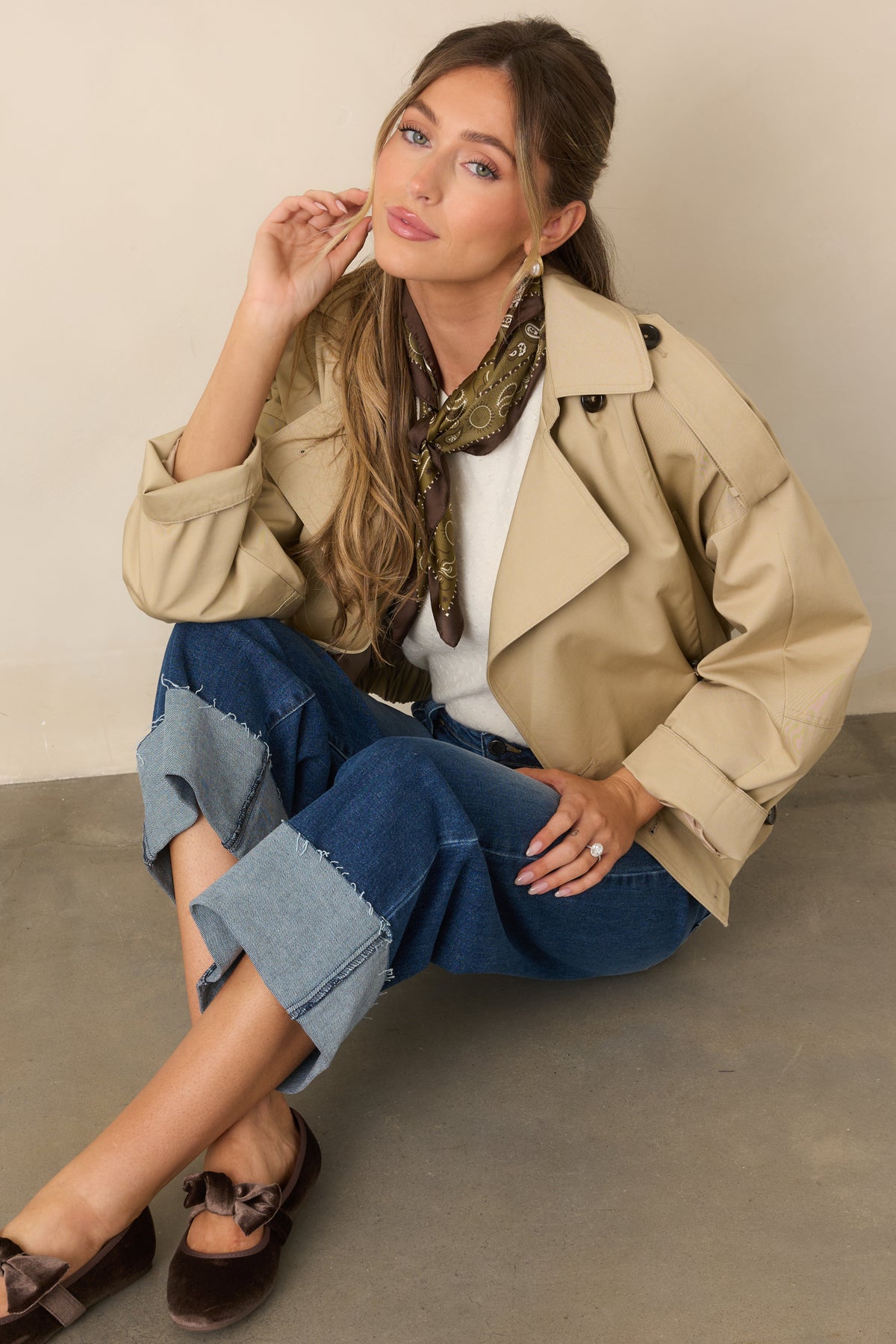 Beige cropped trench jacket with a double-breasted front, tonal buttons, notched lapels, and long sleeves.