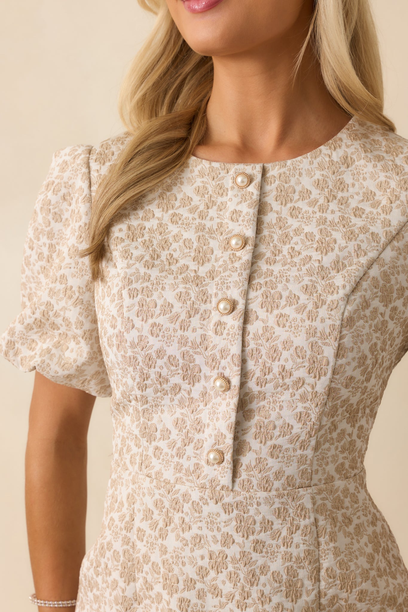 Detailed shot of decorative pearl buttons and floral jacquard texture on the beige fabric.