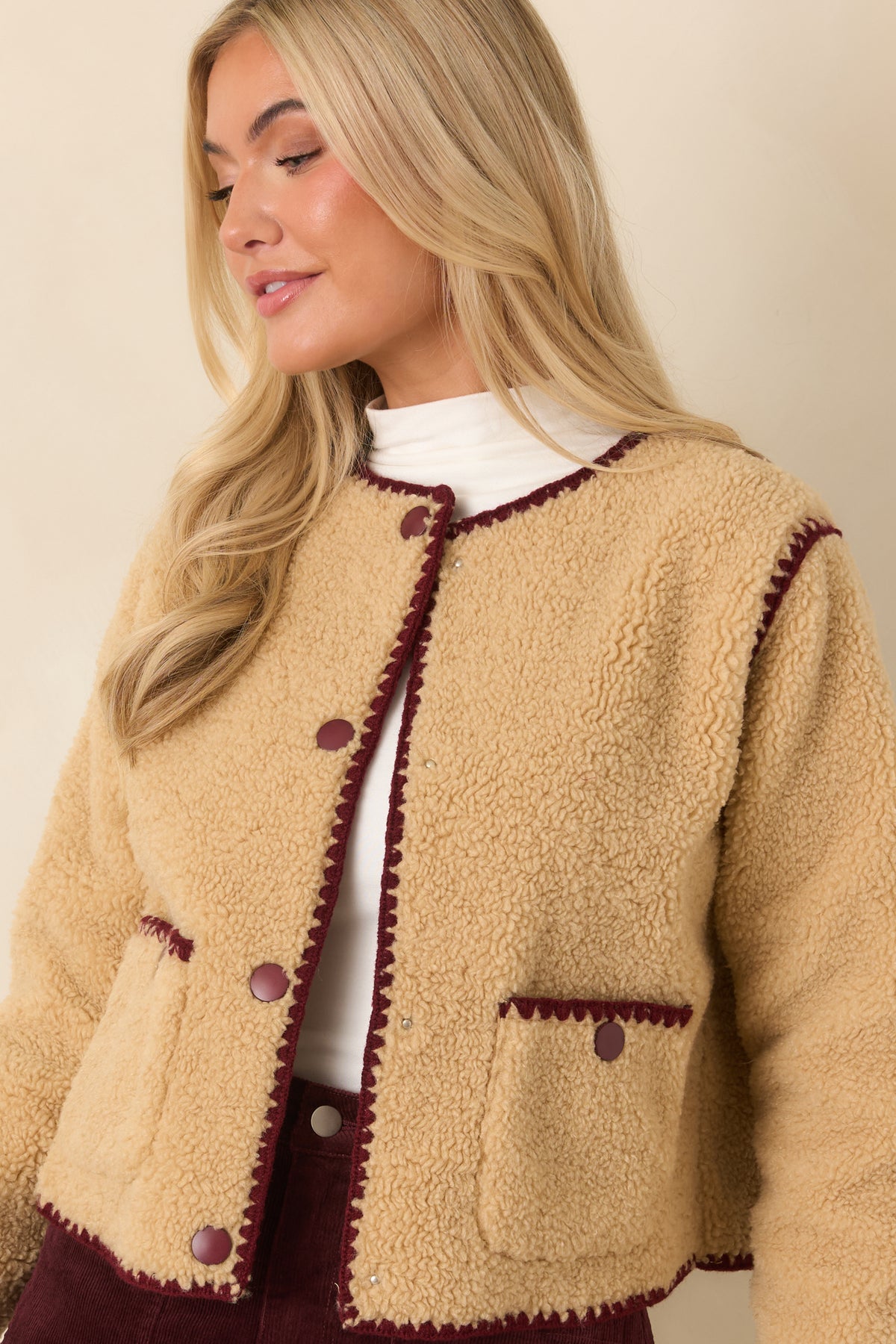 Hip-length beige faux sherpa jacket with a soft textured finish and burgundy trim along the front opening.