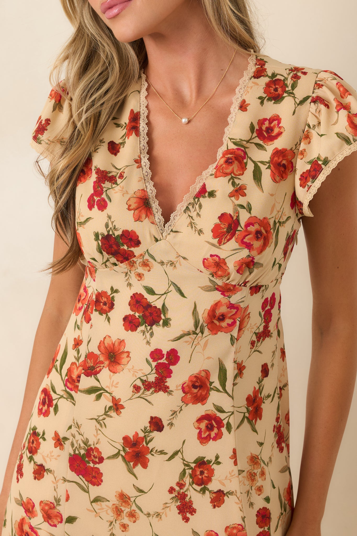 Close-up of the beige floral midi dress highlighting the lace-trimmed V-neckline, flutter sleeves, and colorful botanical print.