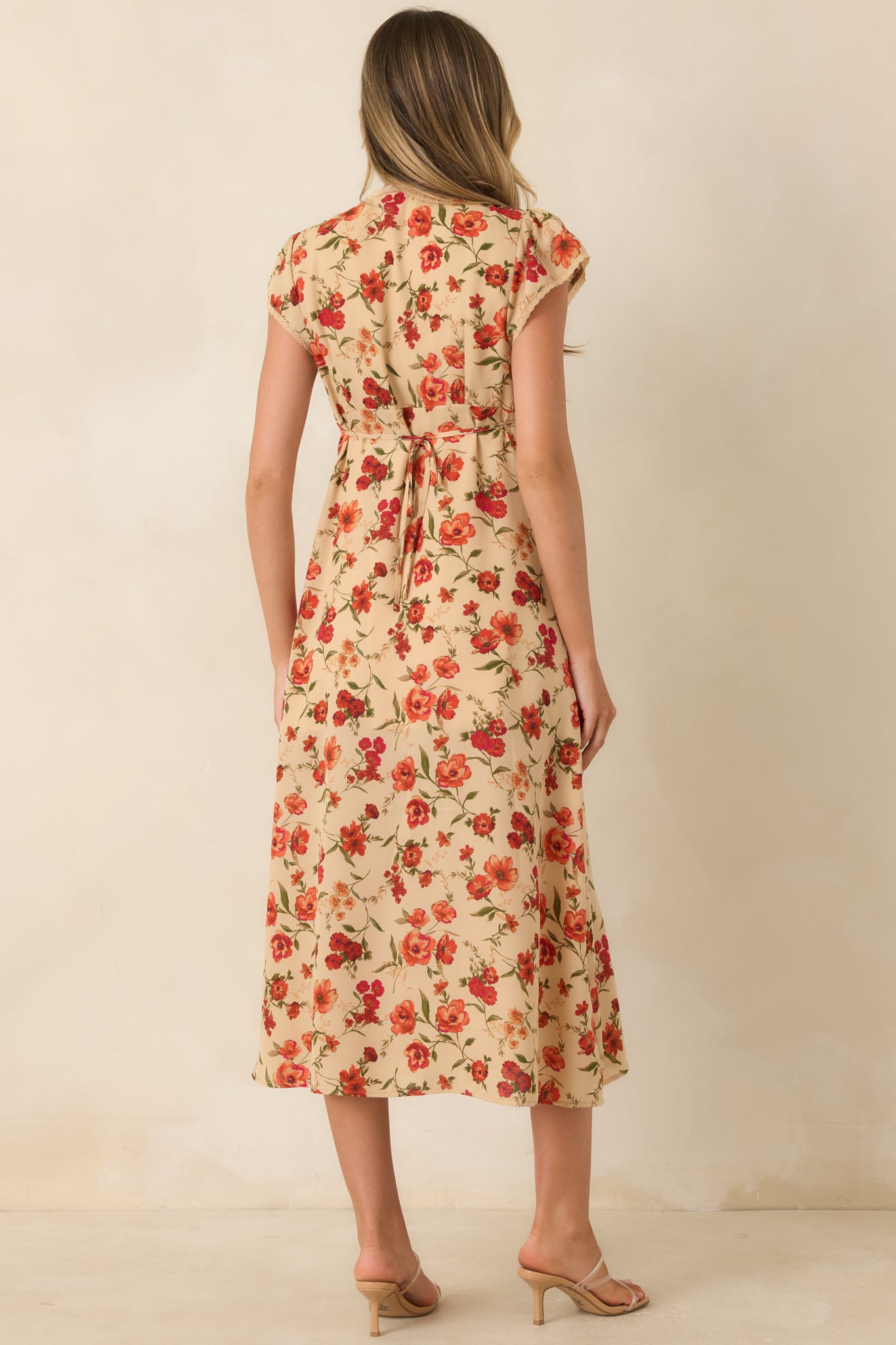 Rear view of the beige floral midi dress featuring the adjustable back tie, flowing skirt, flutter sleeves, and allover floral print.