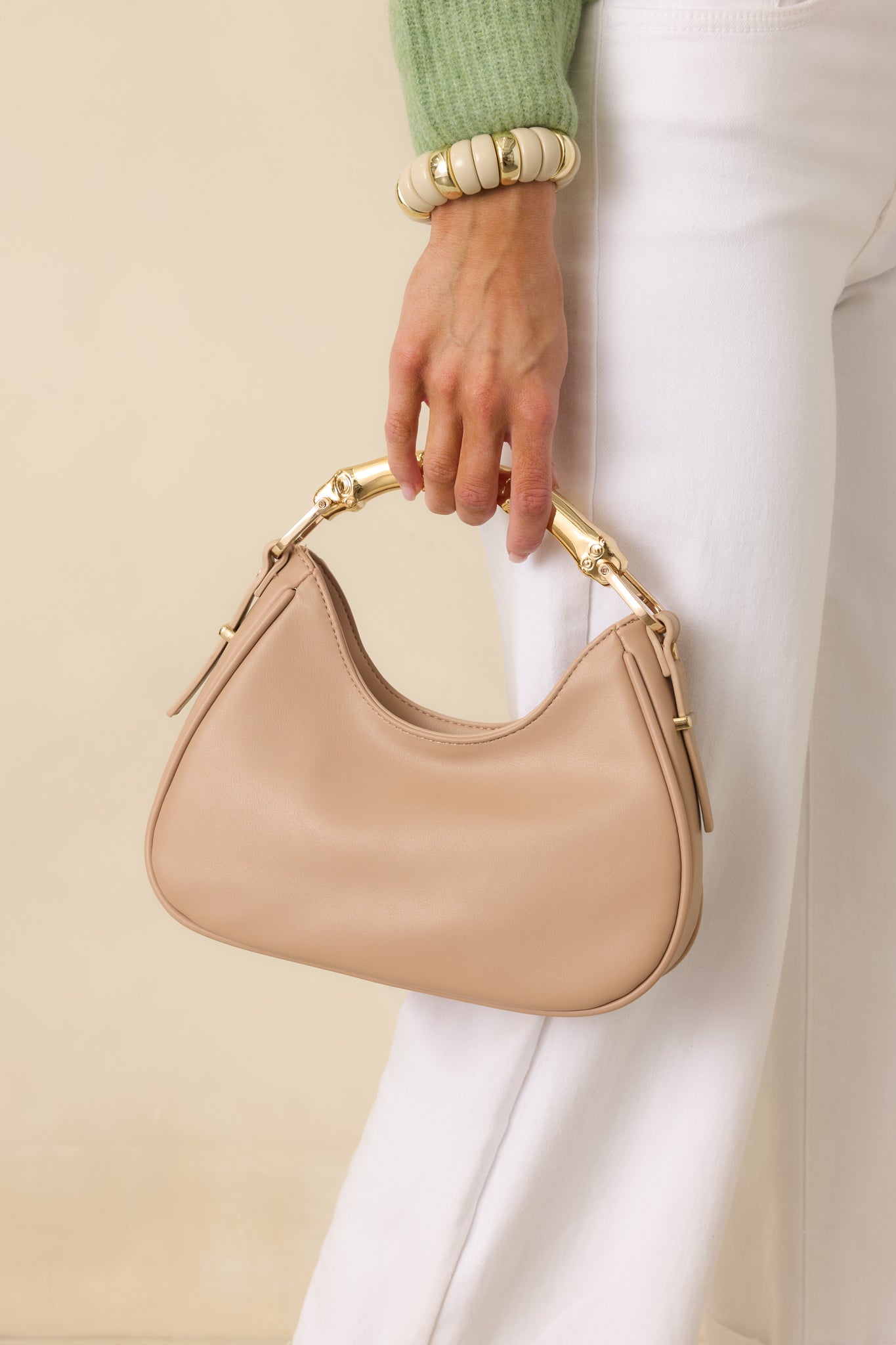 Front view of the beige handbag showing the smooth faux leather exterior, structured silhouette, and gold-tone bamboo-inspired top handle.
