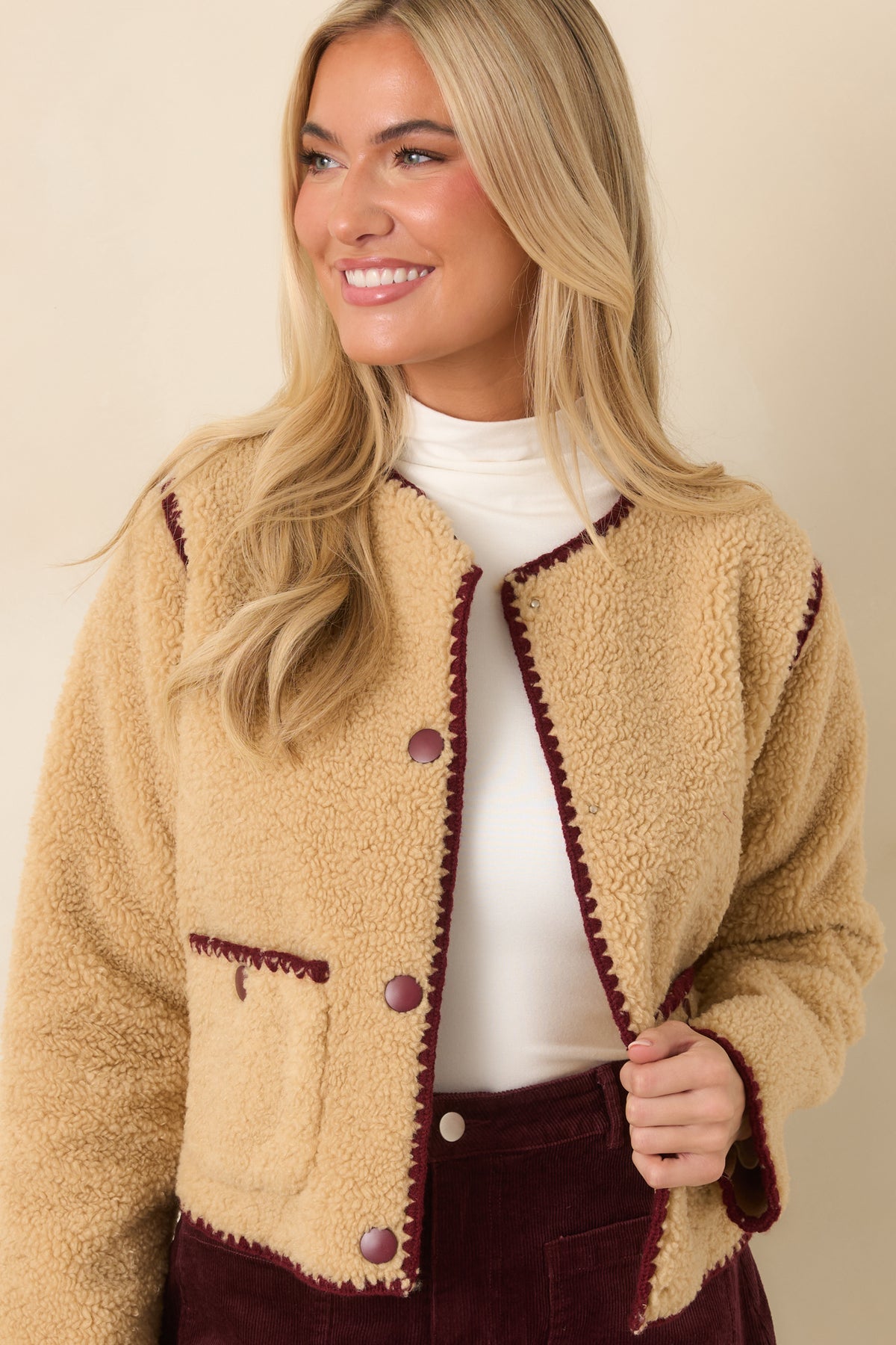 Burgundy contrast stitching highlights the front patch pockets against the fuzzy beige sherpa fabric.