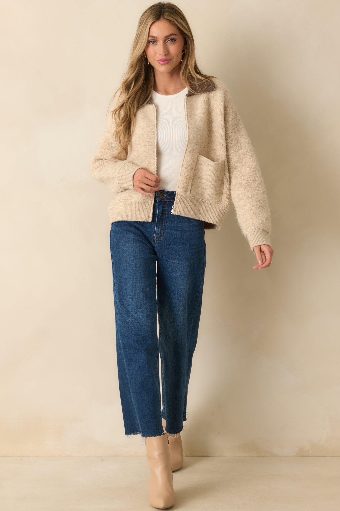 An angled front view of the beige knit jacket showing a relaxed fit and functional front patch pockets.