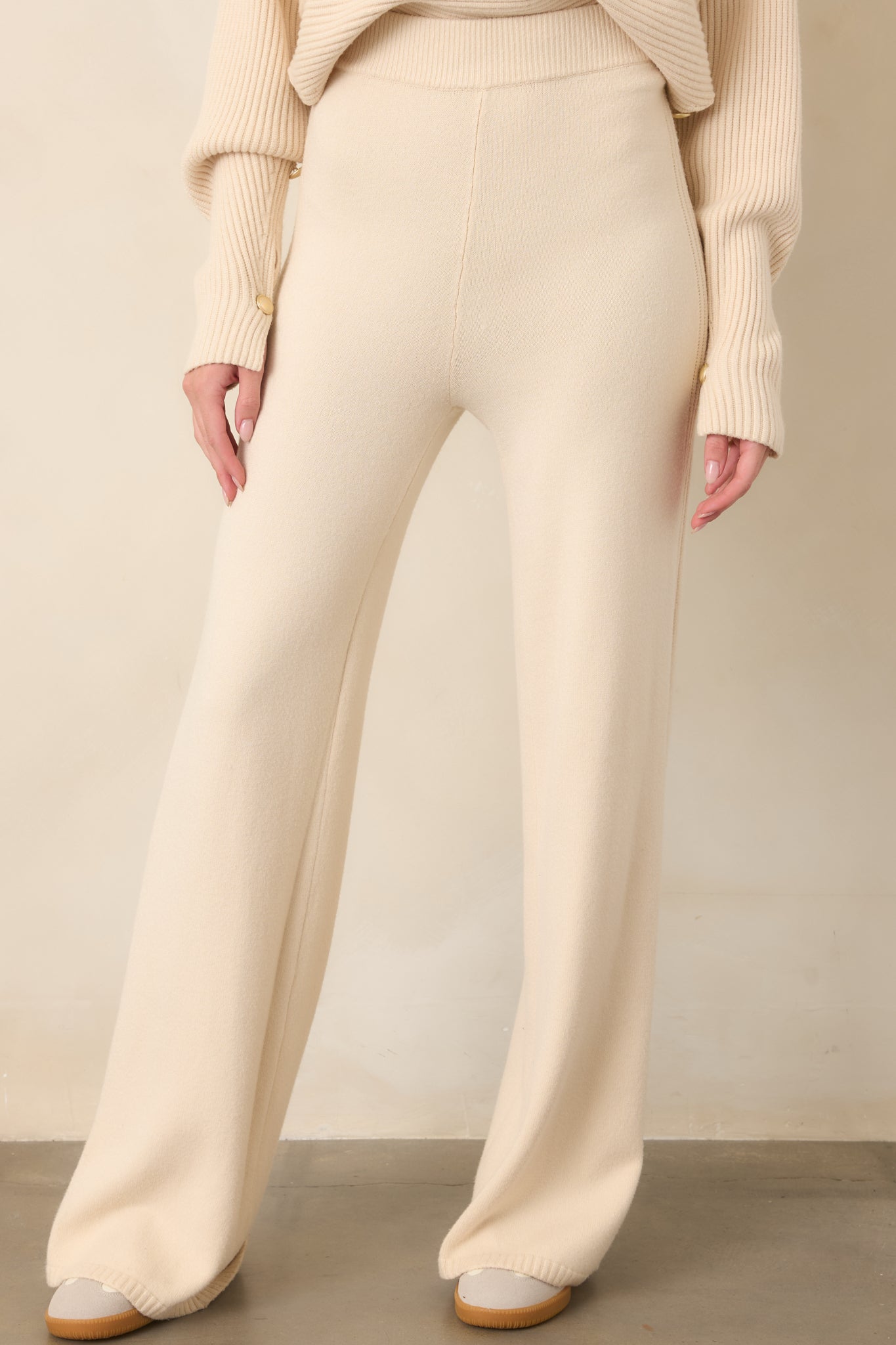 Close view of the beige knit pants showing the high-rise elastic waistband, soft knit texture, and clean seam construction.