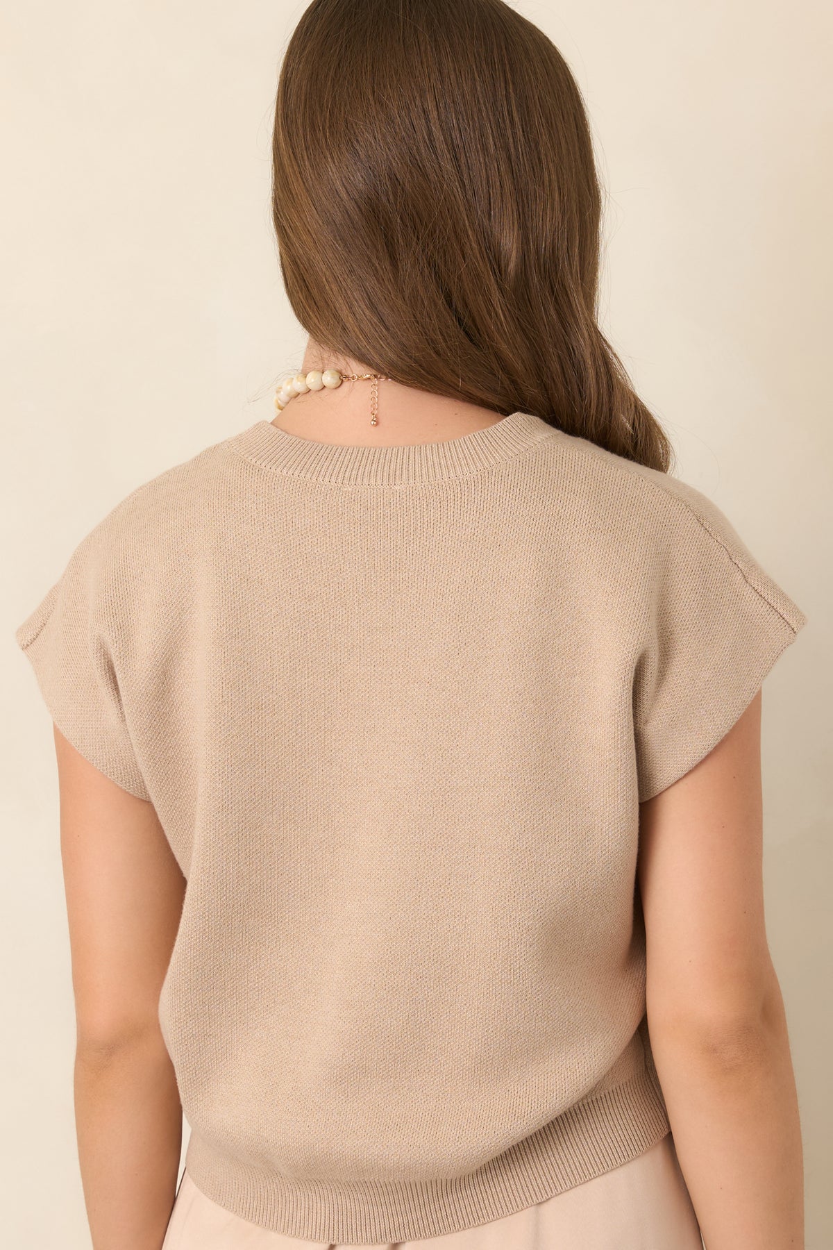 Rear view of the beige knit sweater showcasing its relaxed silhouette, cap-style sleeves, soft fabric, and ribbed hem finish.