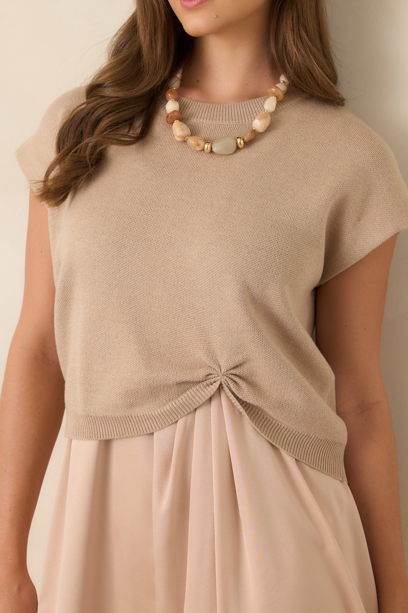 Close-up of the beige knit sweater highlighting its ribbed crew neckline, soft knit texture, and cap-style sleeve construction.