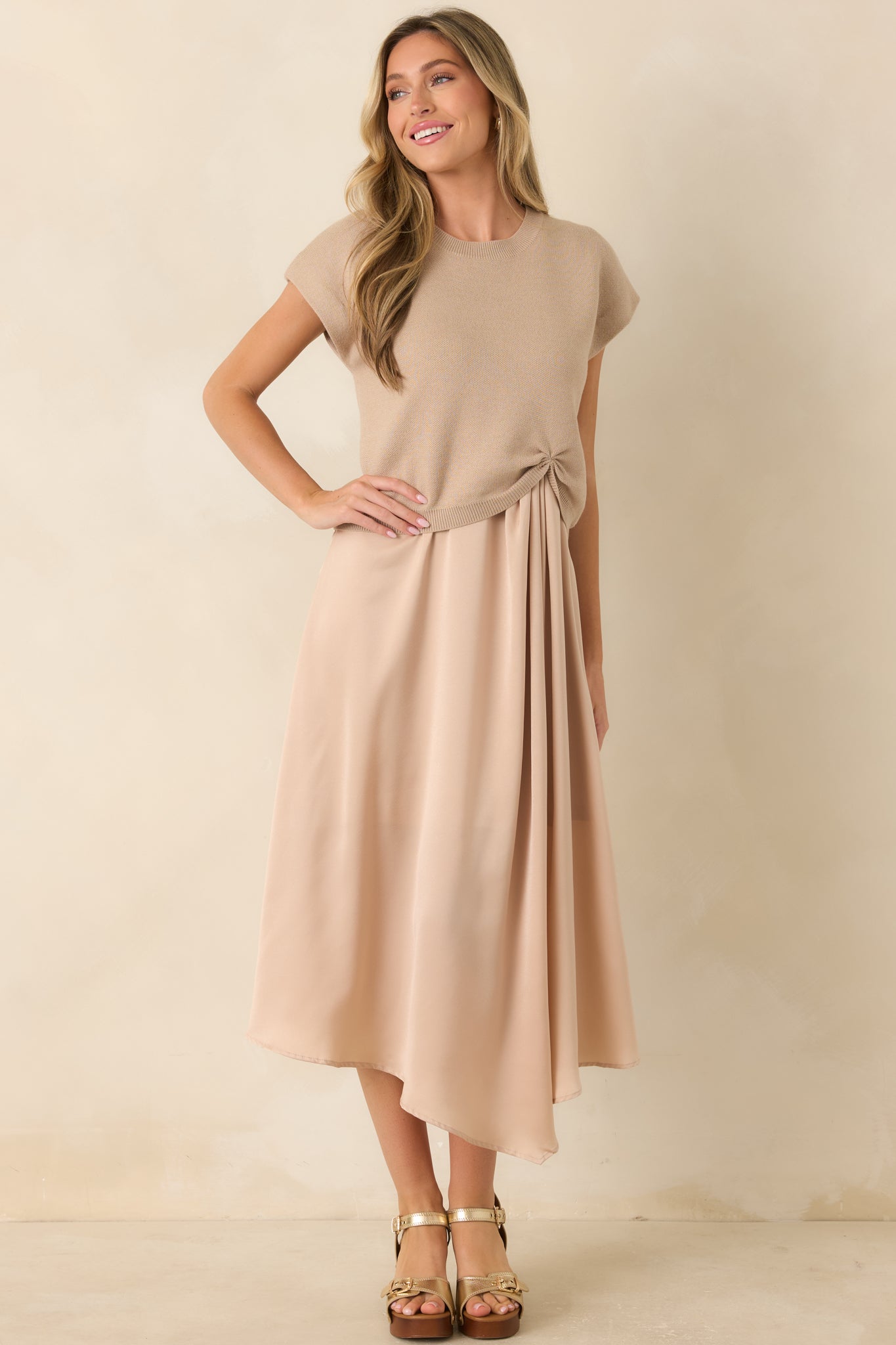 Full-length view of a beige lightweight knit sweater featuring a relaxed silhouette, ribbed crew neckline, cap-style sleeves, and a cinched front hem.
