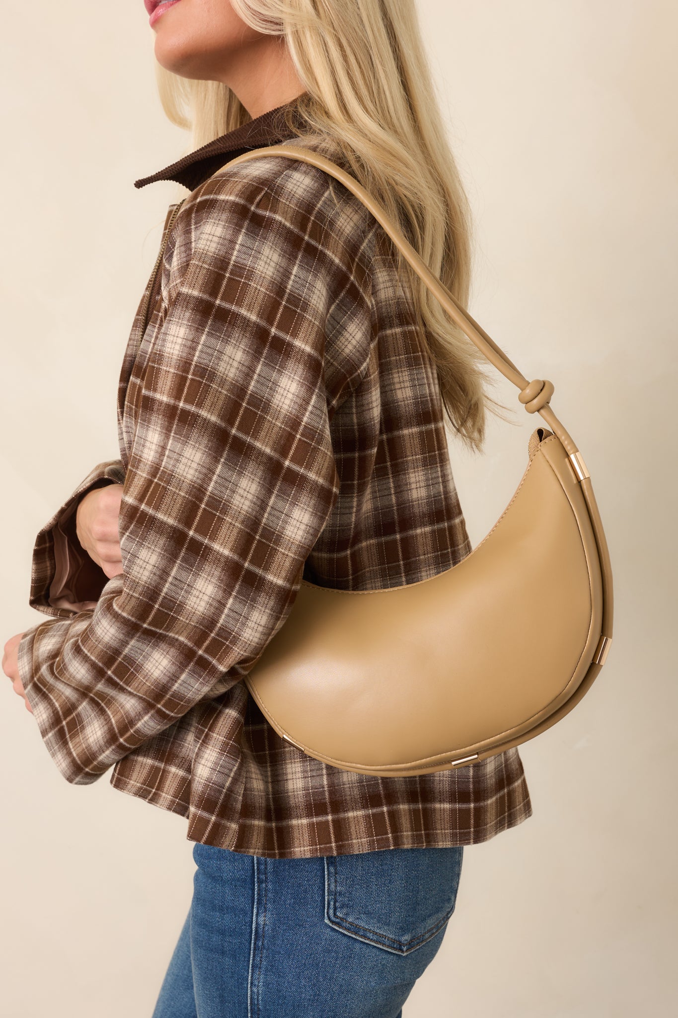 Neutral beige handbag with an adjustable shoulder strap featuring knotted details, polished gold-tone accents, and a secure top zipper closure.