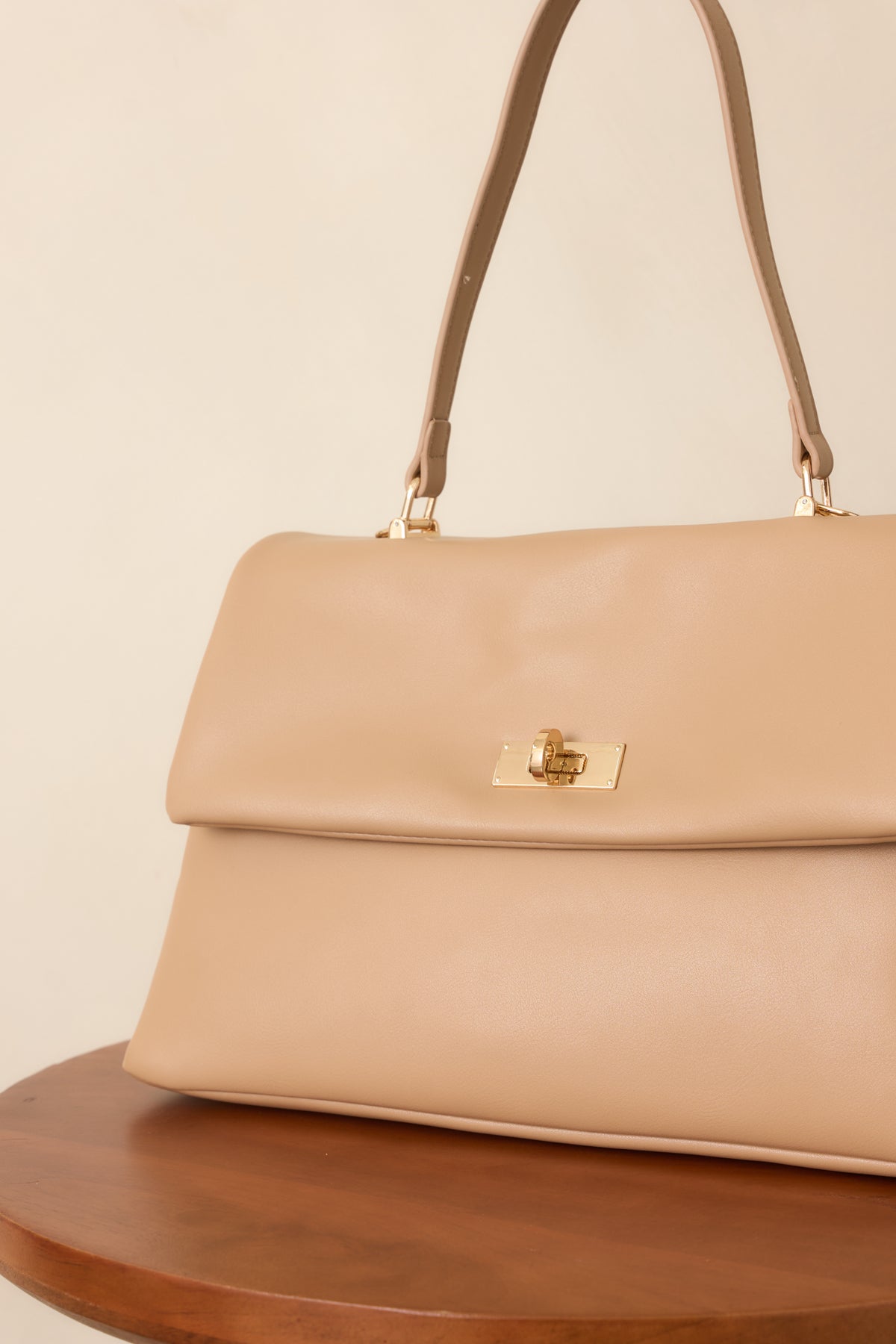 Beige leather handbag detail highlighting the gold-tone hardware and twist-lock closure.