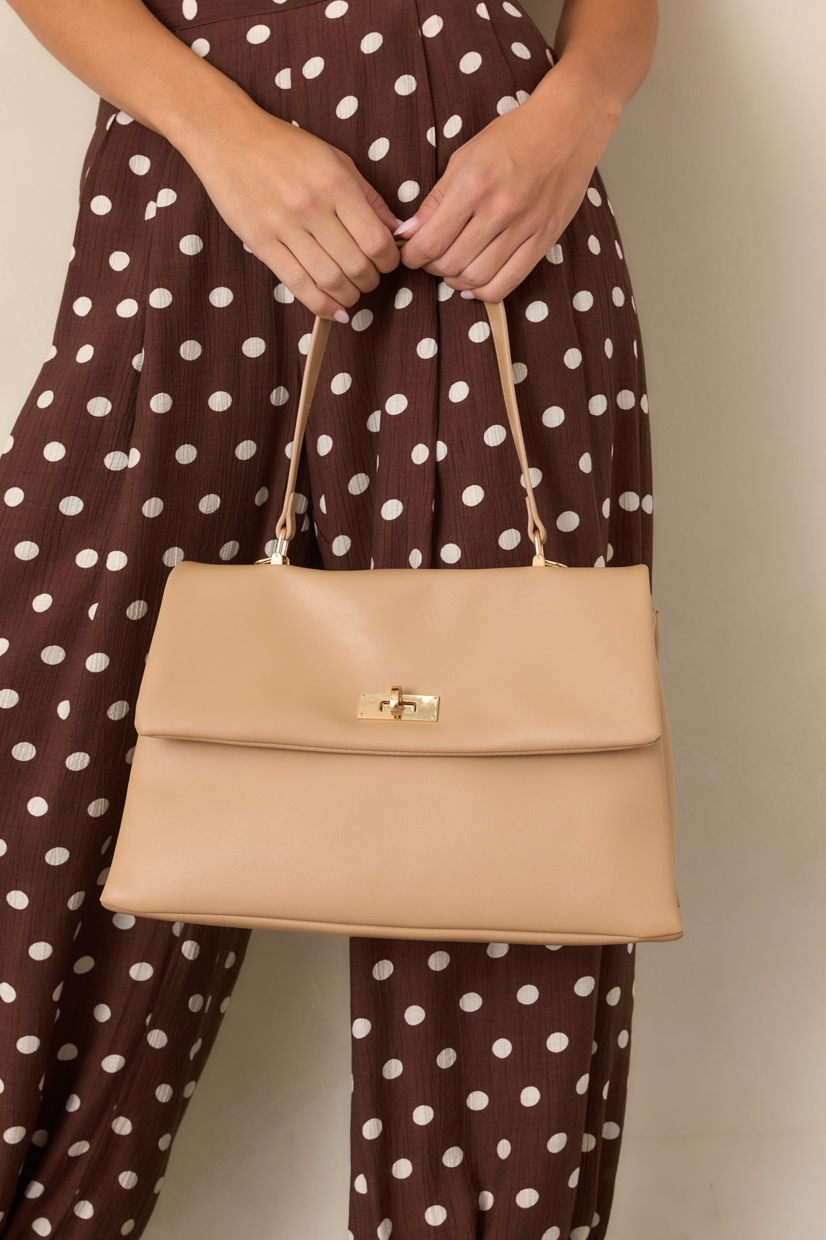 Beige leather handbag highlighting the gold-tone twist-lock hardware on its flap closure.