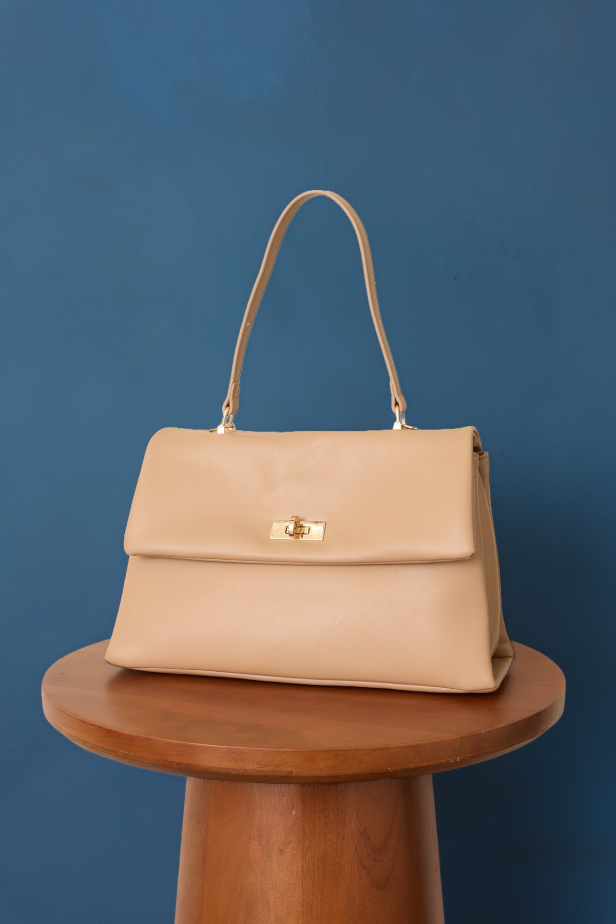 Structured beige leather handbag featuring gold-tone hardware, a flap top, and twist-lock closure.
