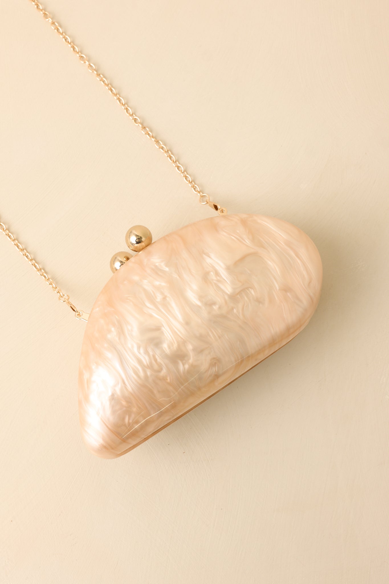 Beige marble clutch featuring a structured oval silhouette, smooth marbled exterior, gold-tone hardware, and chain strap.