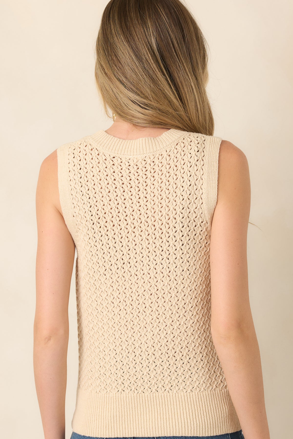 Rear view of the beige sleeveless top showcasing its open-knit construction, round neckline, and ribbed hem and armhole trim.