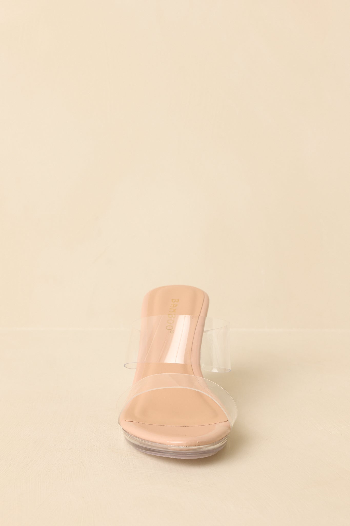Front-facing view of beige open-toe platform heels against a beige background highlighting the clear strap and platform sole.