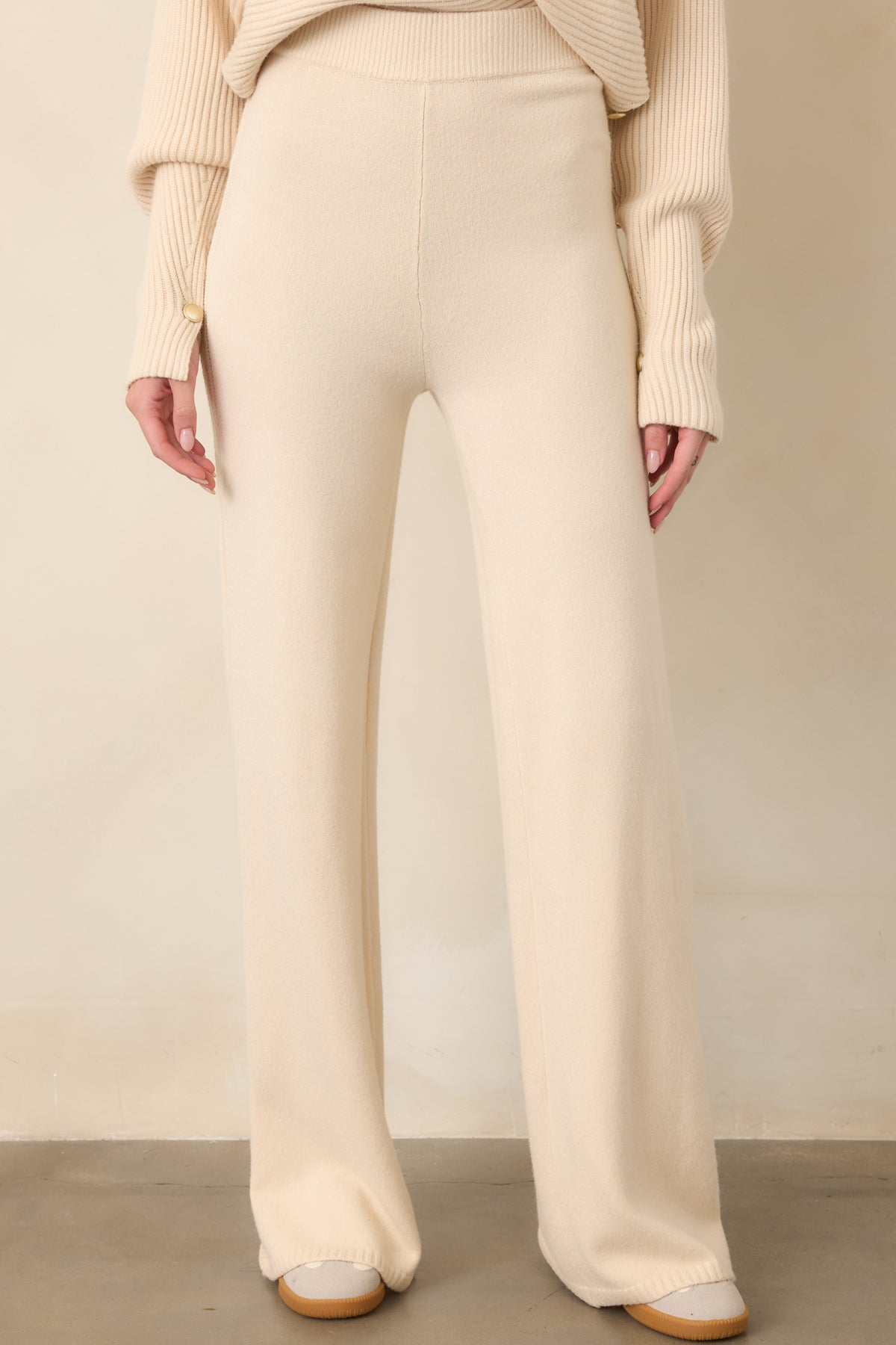 Detailed view of the beige knit pants highlighting the smooth fabric, wide-leg construction, and subtle ribbed texture along the outer seam.