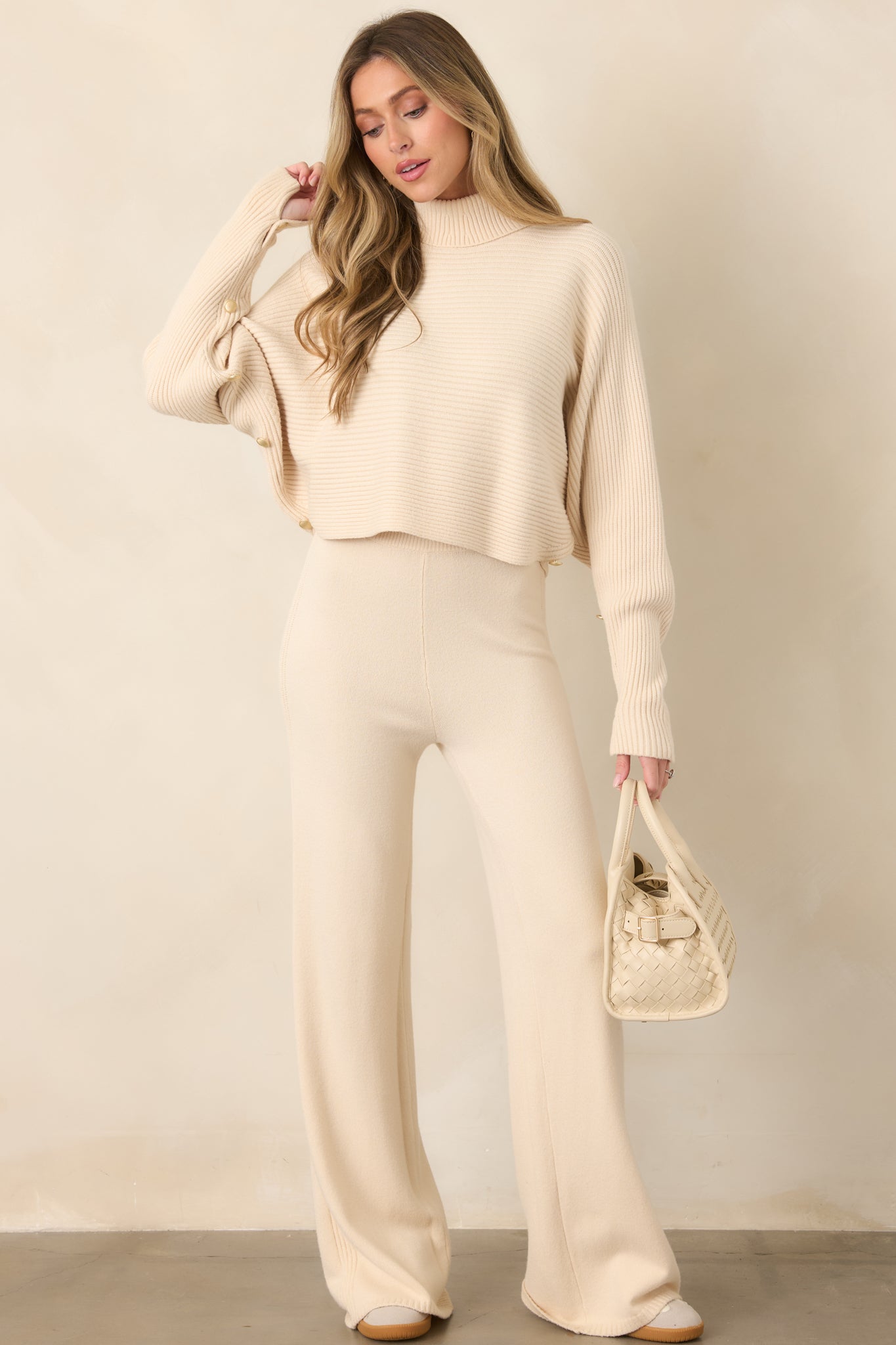Beige ribbed knit sweater with a cozy turtleneck, relaxed batwing sleeves, button-accented cuffs, and a cropped hemline.