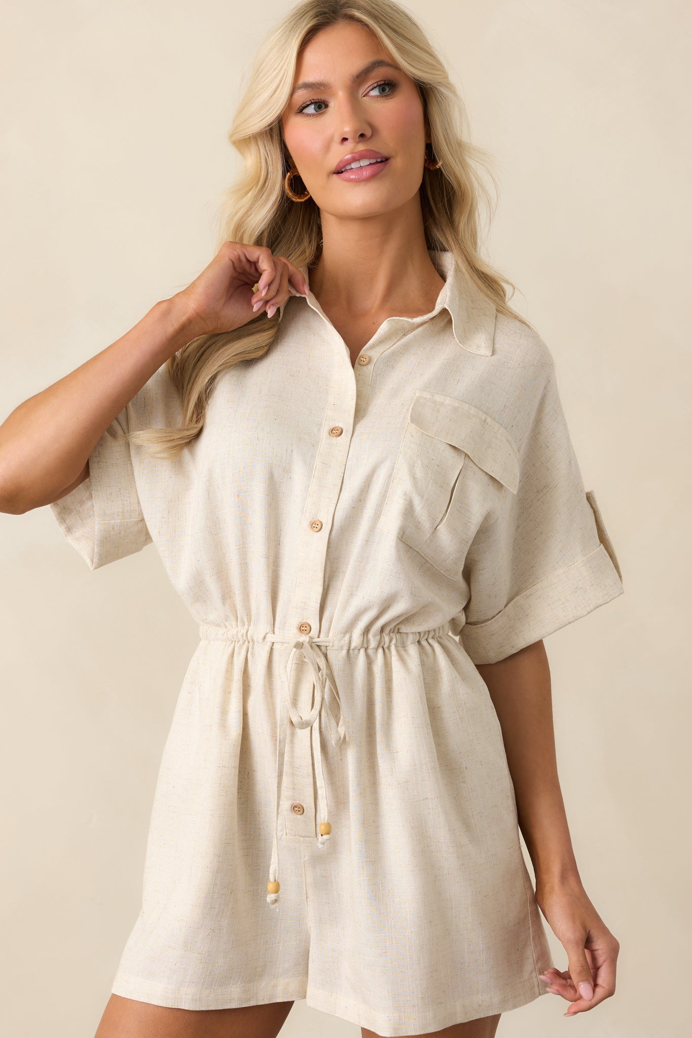 Midsection detail of the romper emphasizing the adjustable drawstring waistband with wooden bead tassels and subtle fabric texture.