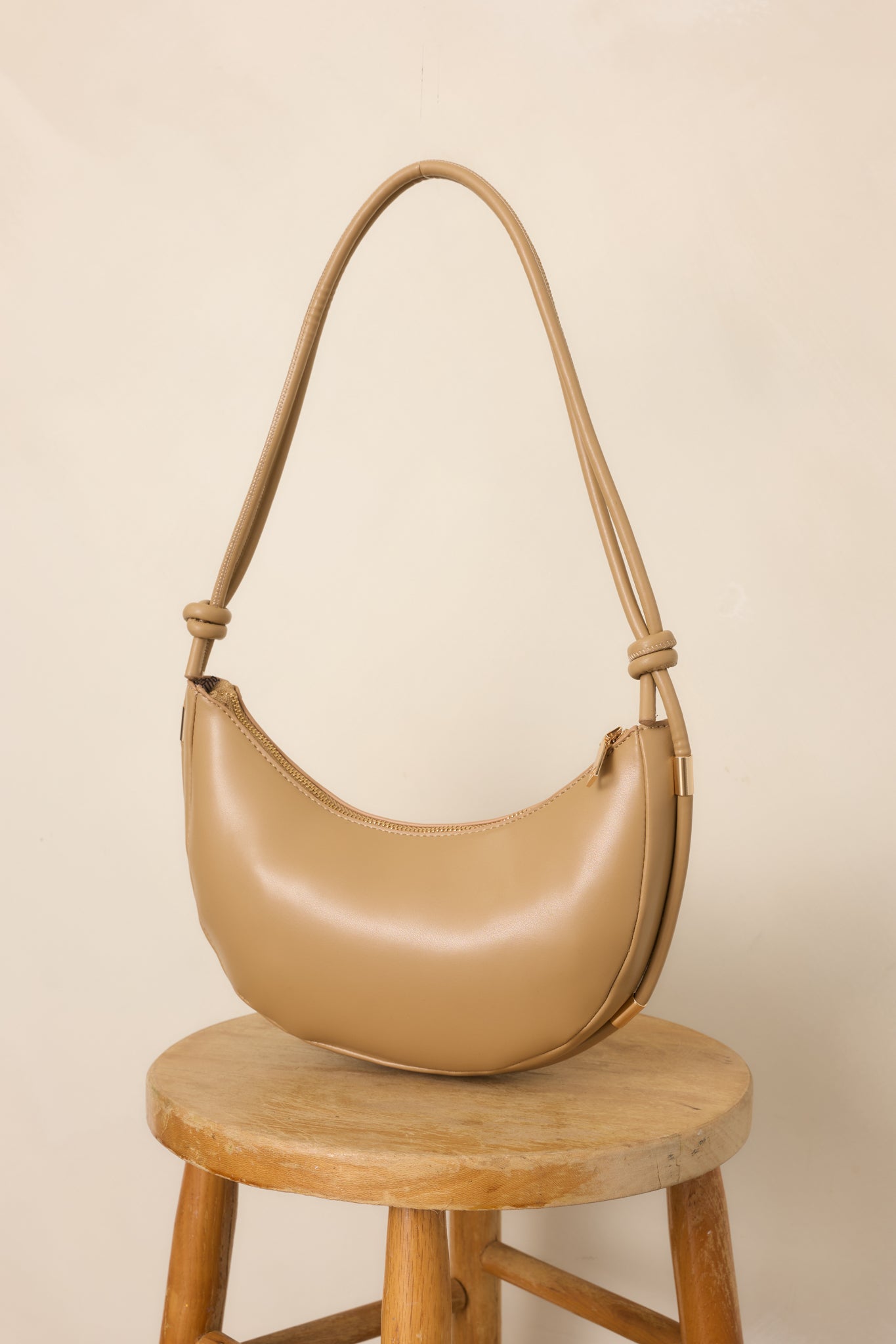 Neutral beige handbag with a roomy silhouette, adjustable knotted shoulder strap, polished gold-tone accents, and secure top zipper closure.
