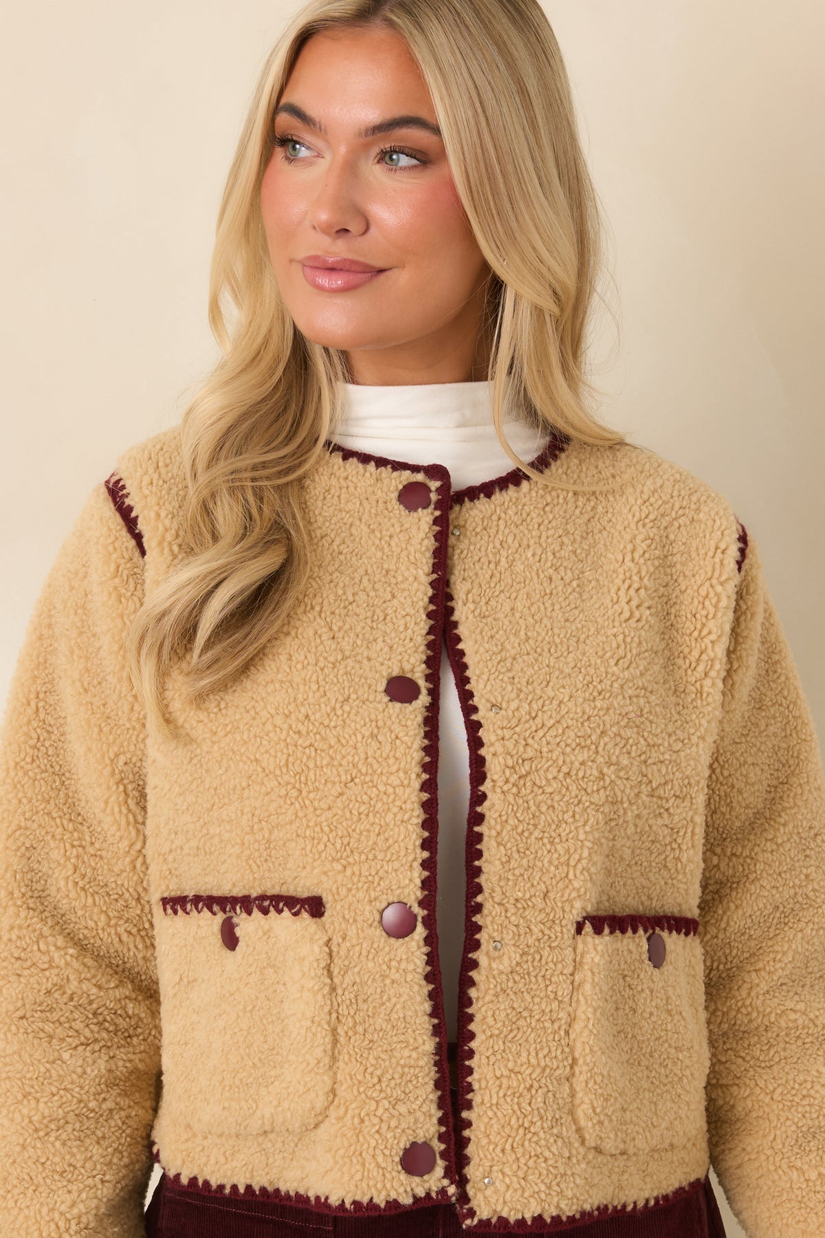 Snap-button closure runs down the front of the beige jacket beneath its rounded crew neckline.