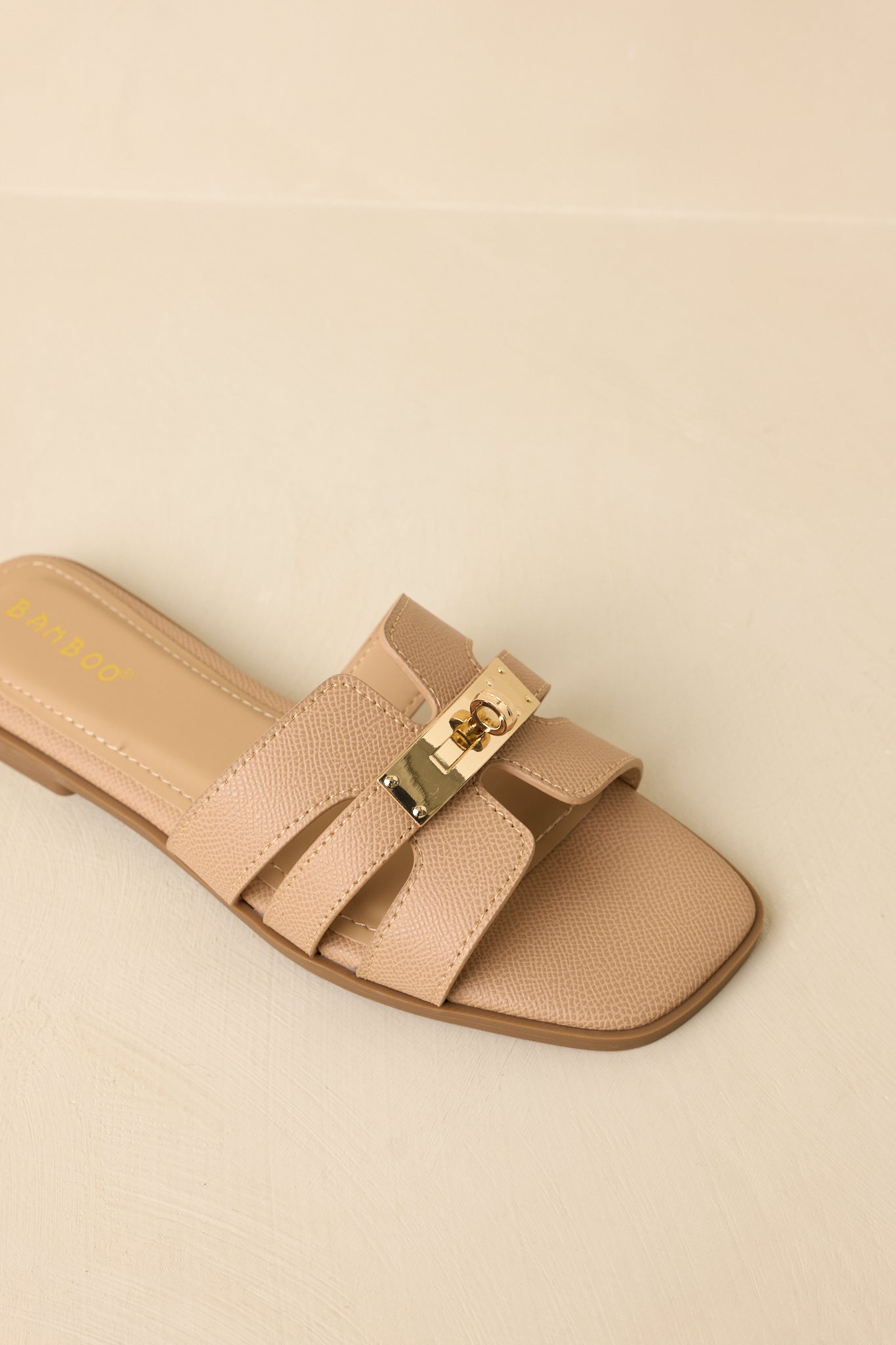 Cropped view of beige slide sandals highlighting textured faux leather straps and gold-tone hardware detail.