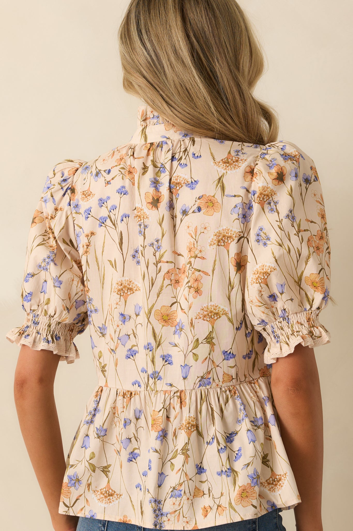 Rear view of beige top showing peplum silhouette and smooth floral print fabric.