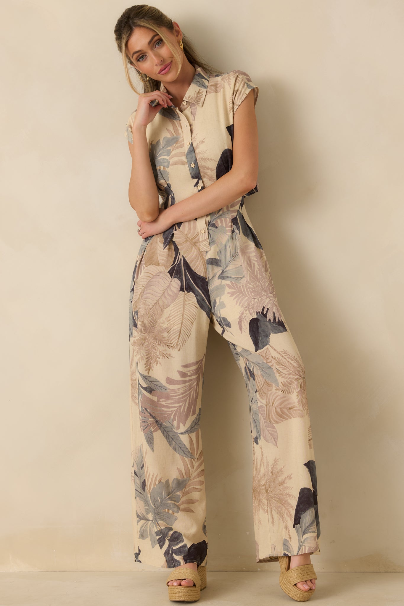 Front view of beige tropical print jumpsuit featuring a structured collar, functional button-front detail, and flowy wide legs.