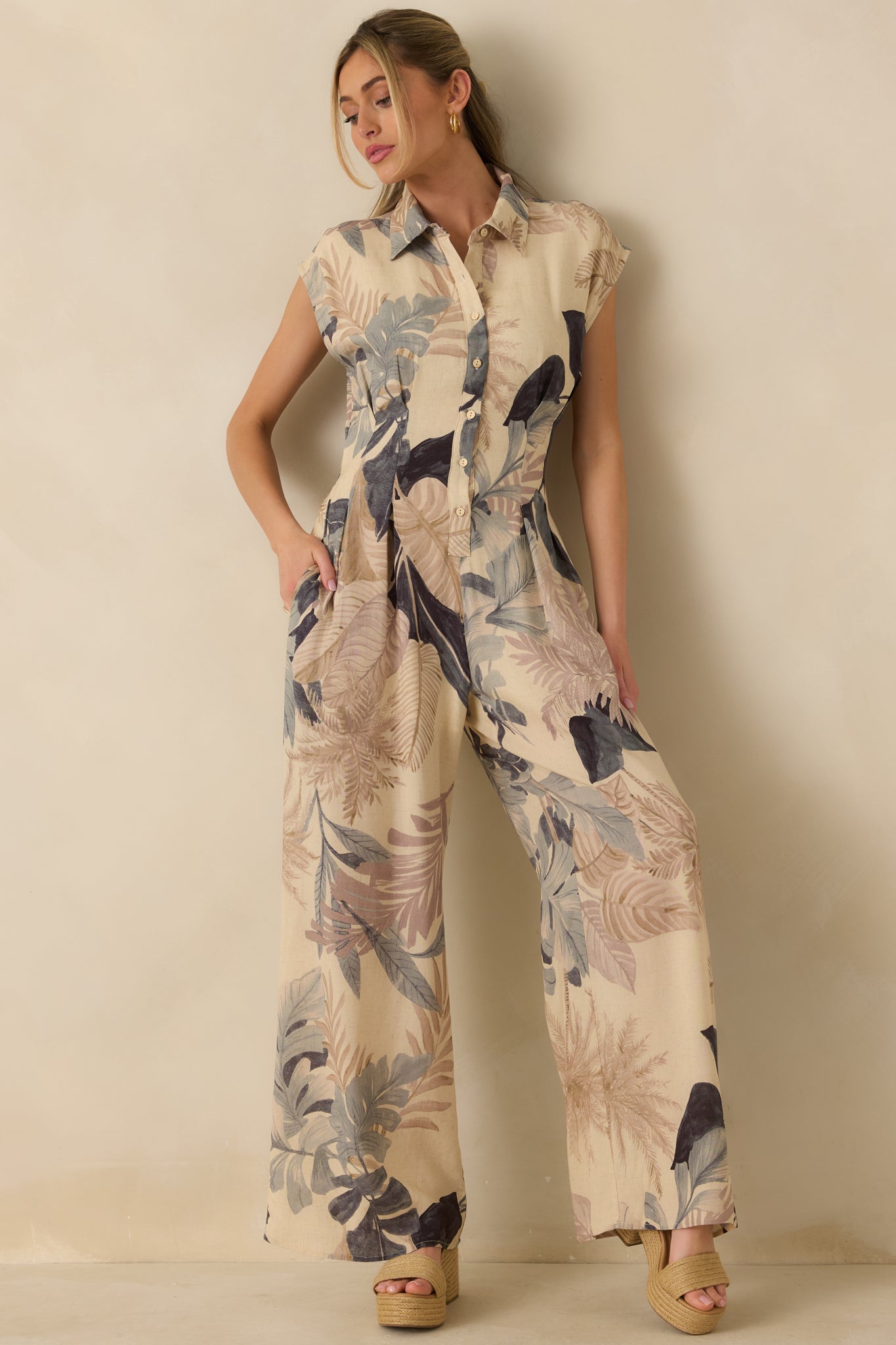 Beige multi tropical print woven jumpsuit with collared button-front bodice, cap sleeves, and relaxed wide-leg silhouette.