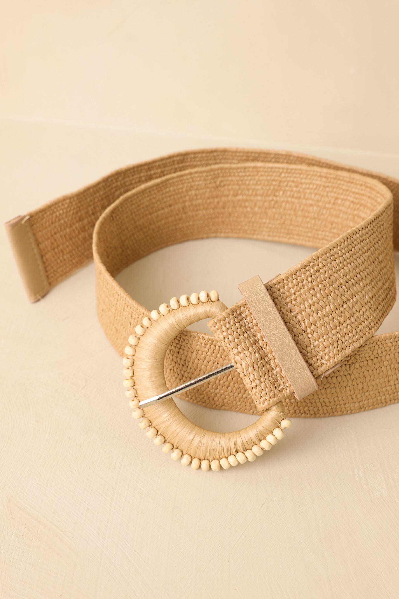 Beige woven belt with a decorative round buckle on a beige background