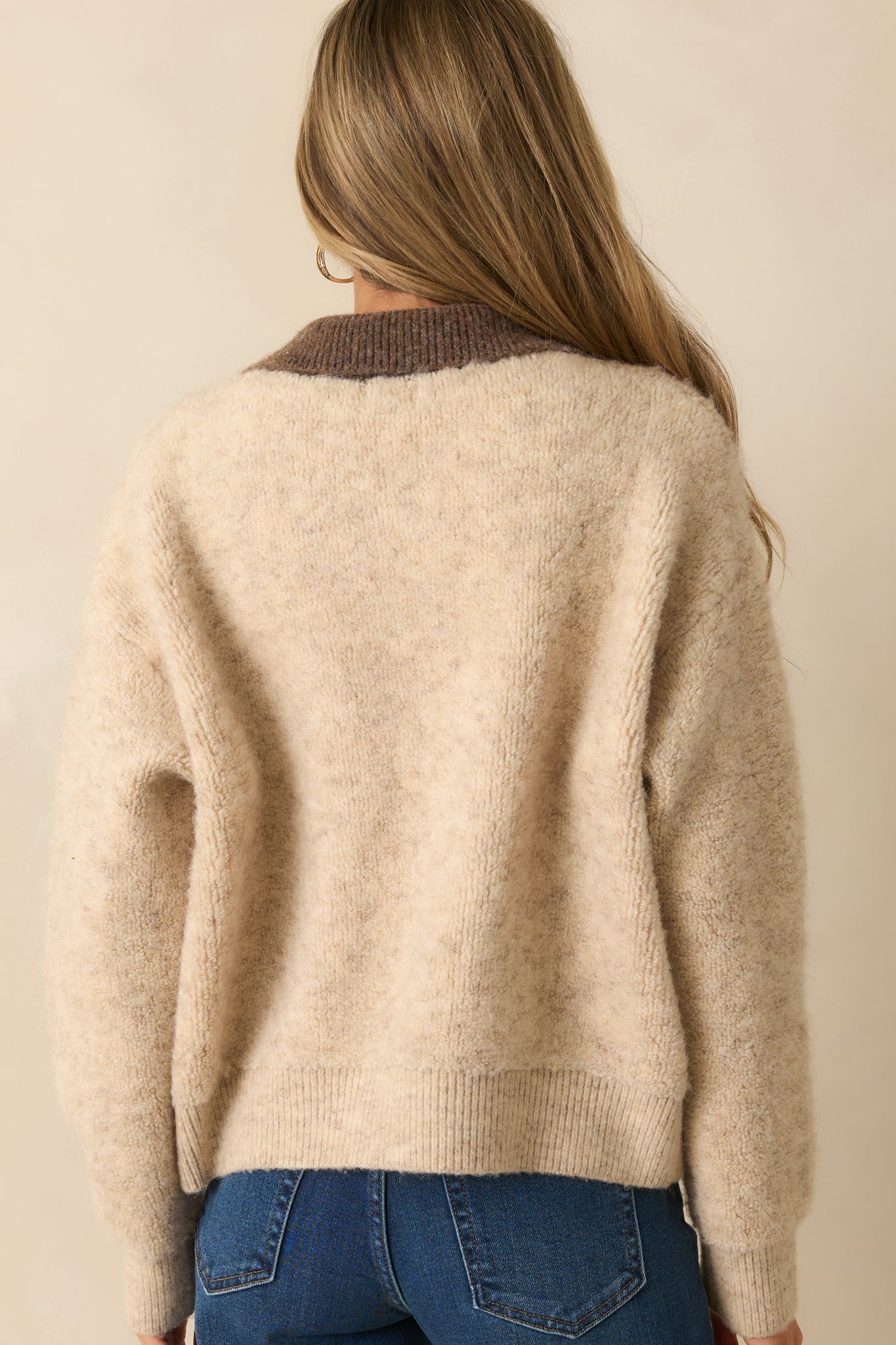 A back view of the beige zip-up jacket featuring a relaxed fit, ribbed hem, and soft knit texture.