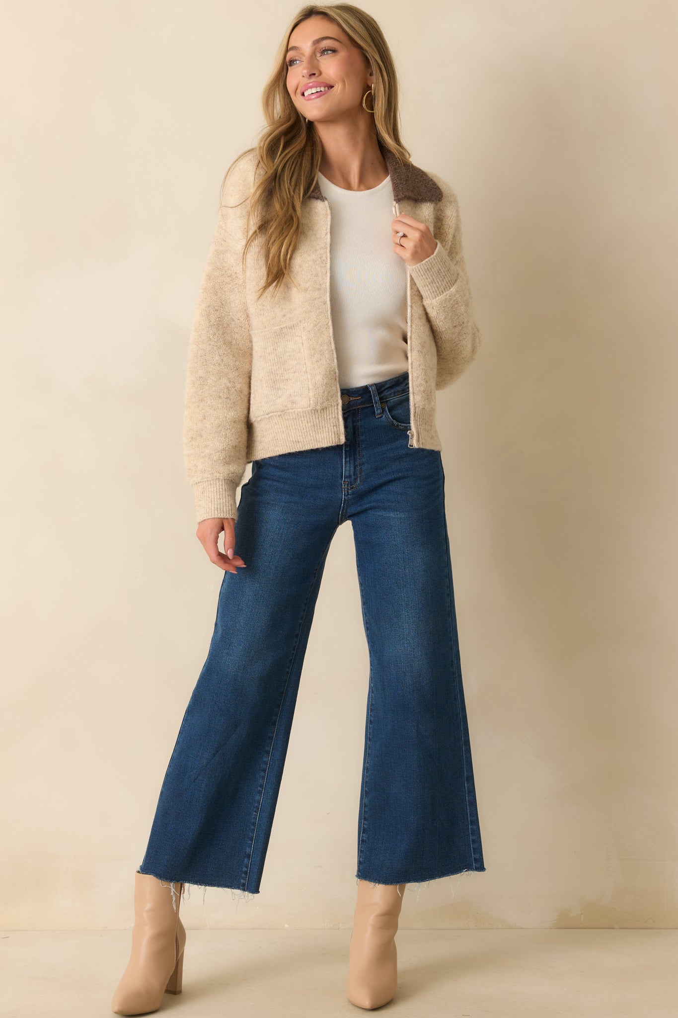 A full body view highlighting the ribbed cuffs and hem of the beige zip-up jacket with brown collar detail.